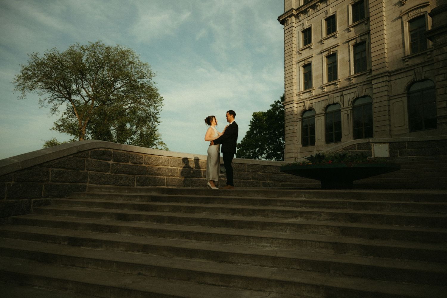 Couple standing on grand stone steps of historic building at dusk during engagement photo session.
