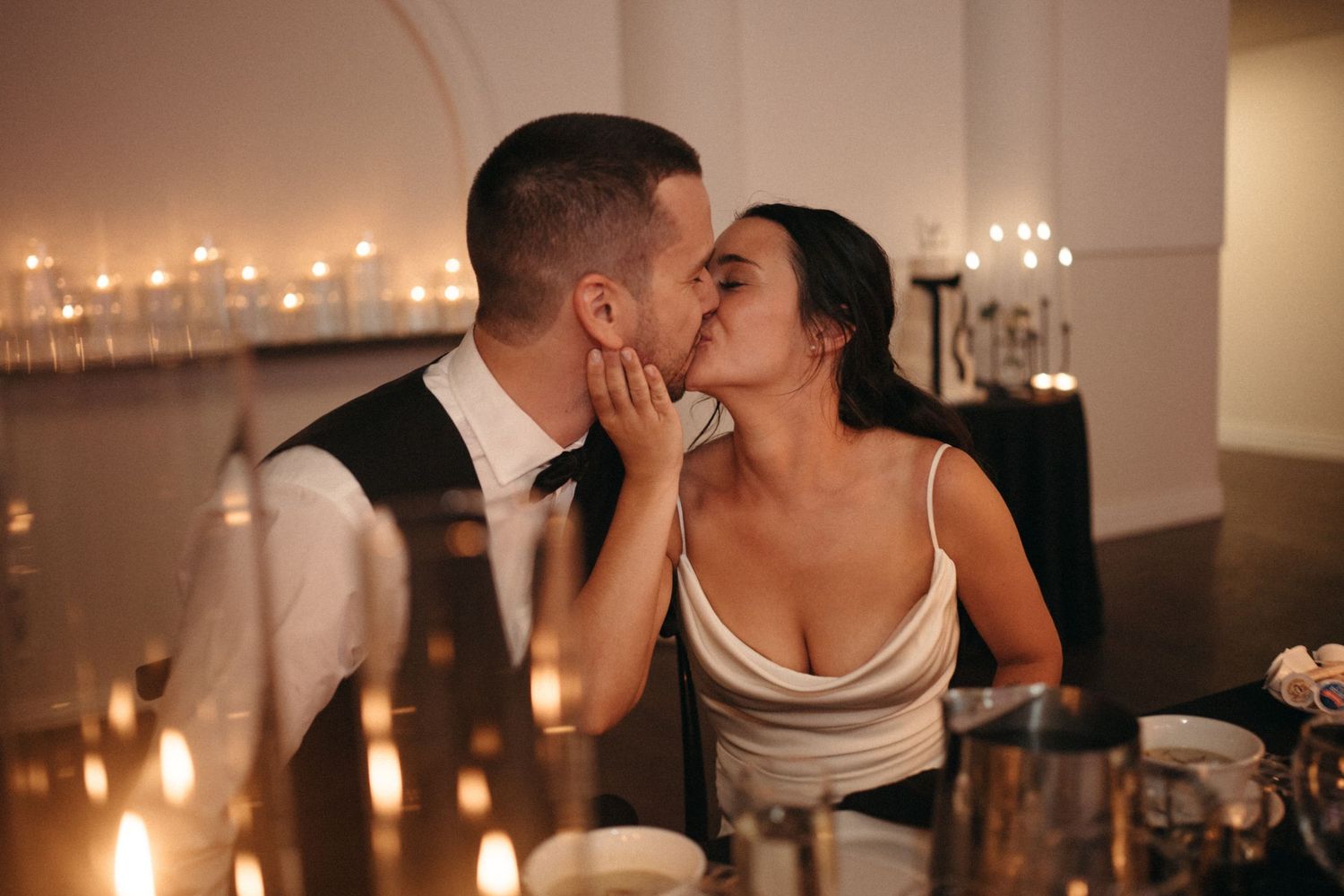 Bride and groom share a romantic candlelit kiss at their wedding reception dinner table.