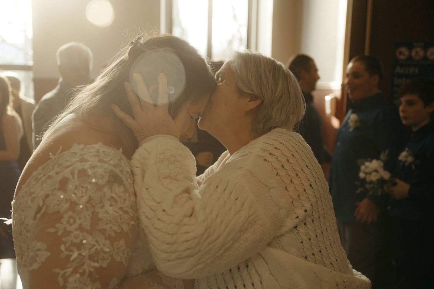 Two brides share a first kiss at their wedding ceremony, bathed in warm sunlight.