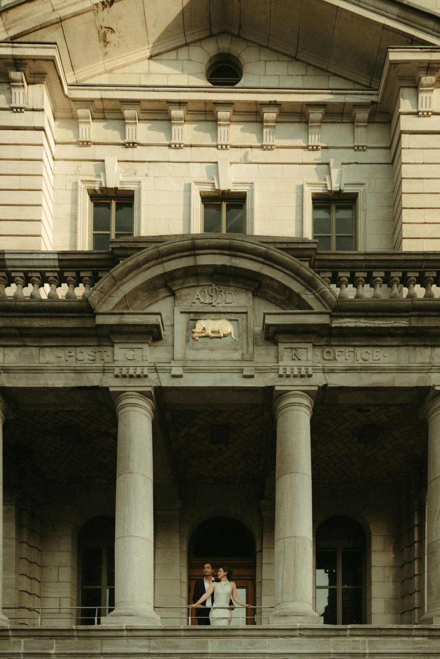 Couple stands between grand neoclassical columns of a historic post office building during their wedding day.
