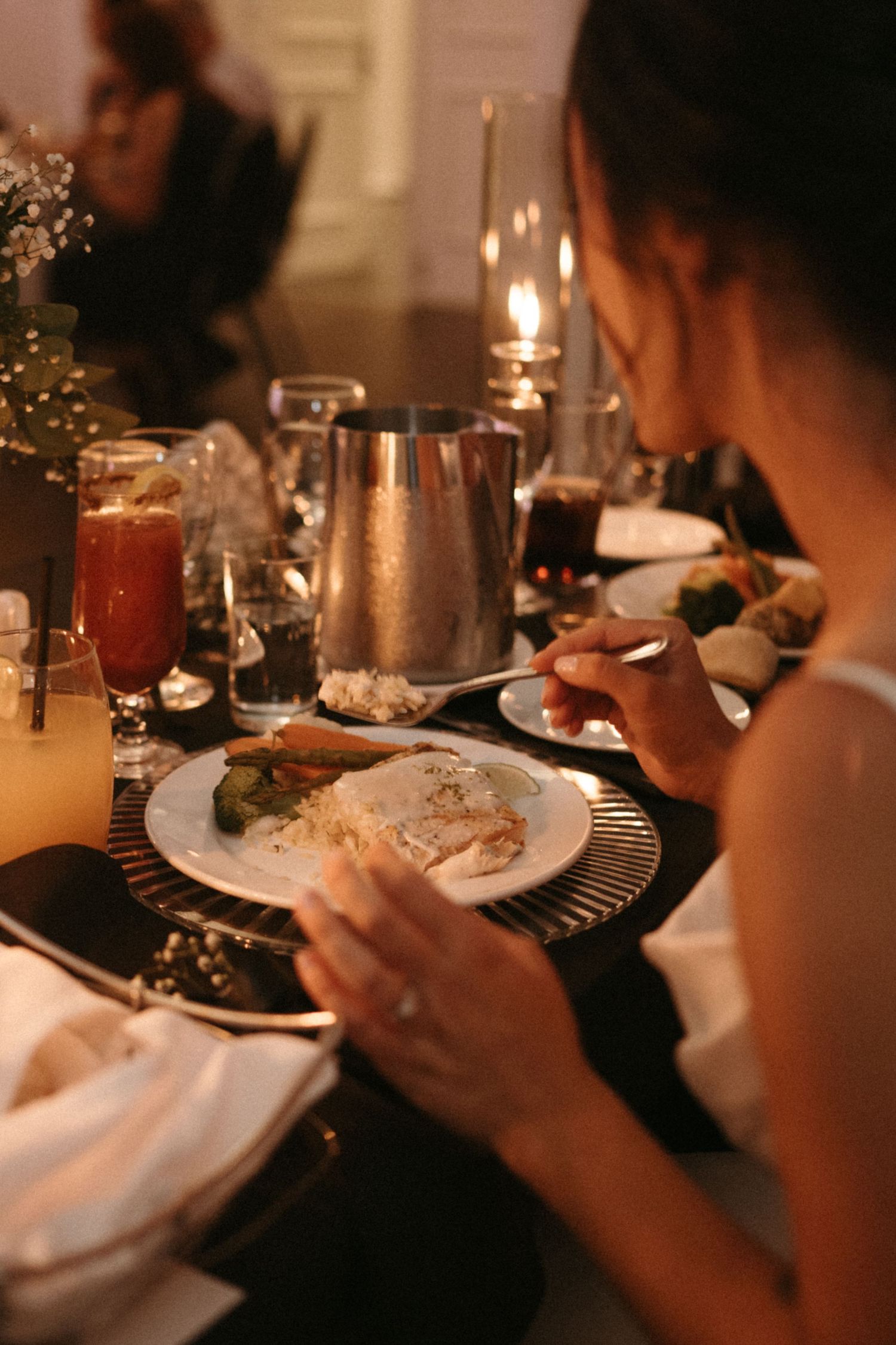 Bride eating dinner at candlelit wedding reception table with elegant place settings and drinks.