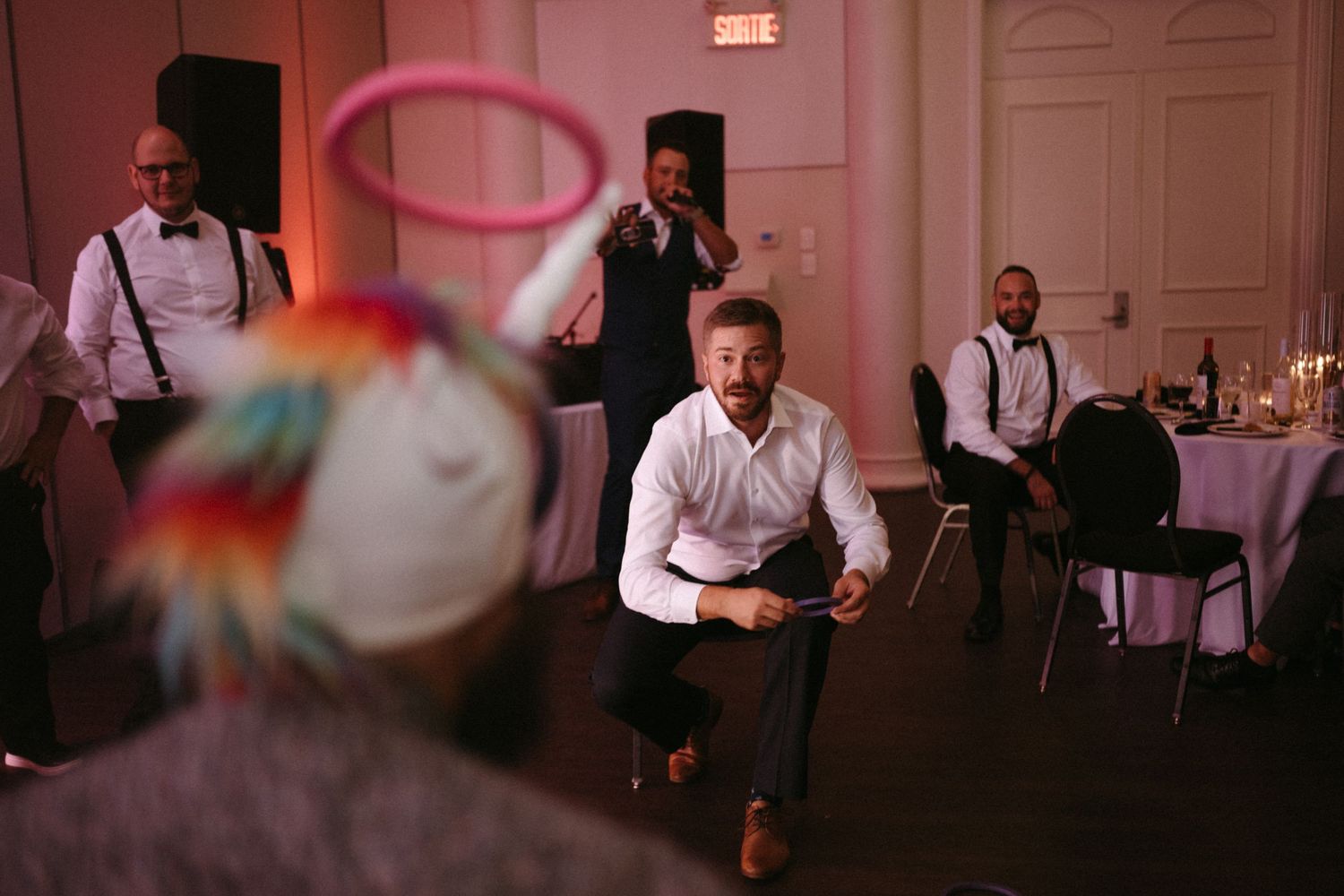 Wedding guest kneeling during a fun reception game with colorful props and guests watching.