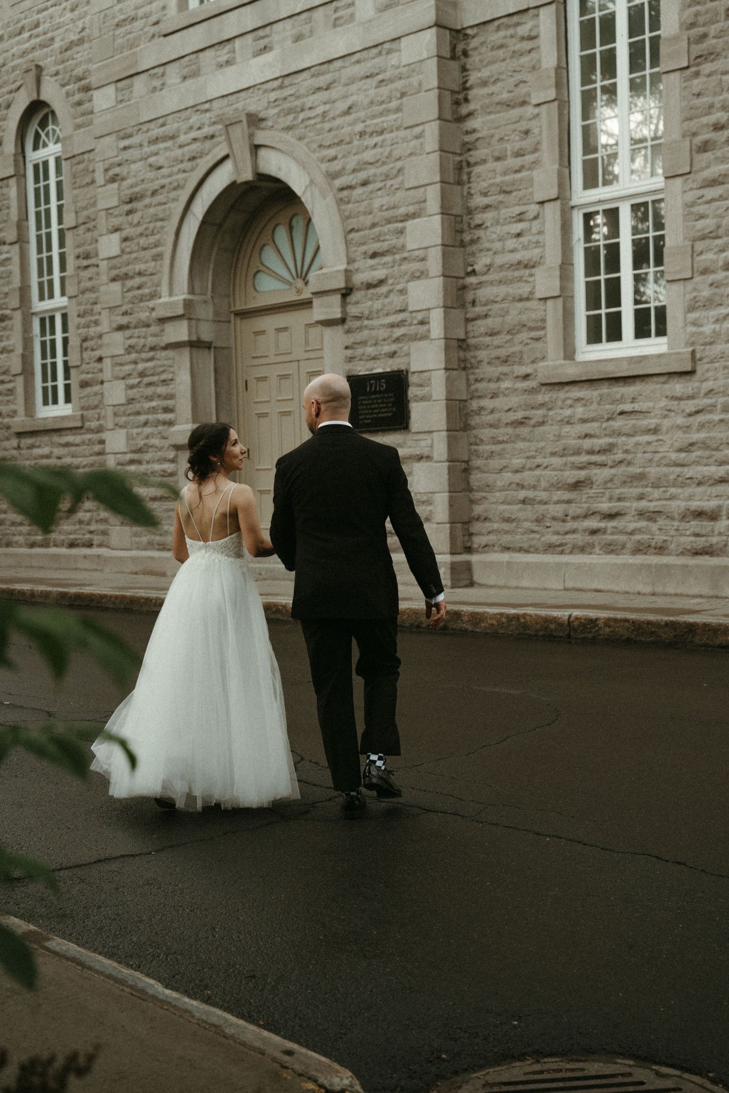 Bride and groom walking hand in hand toward a historic stone church on their wedding day.