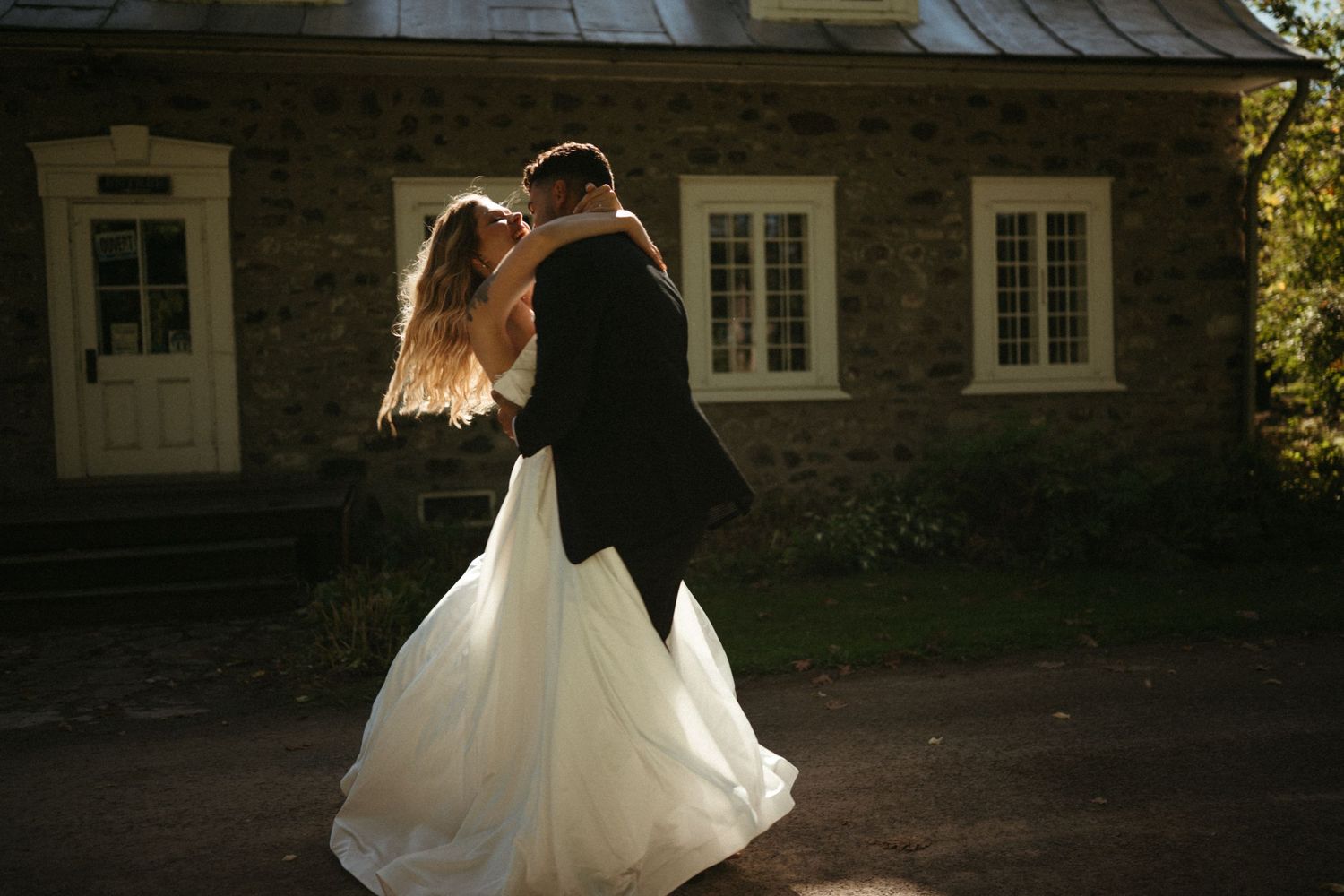 A bride and groom embrace in front of a rustic wooden house at night.