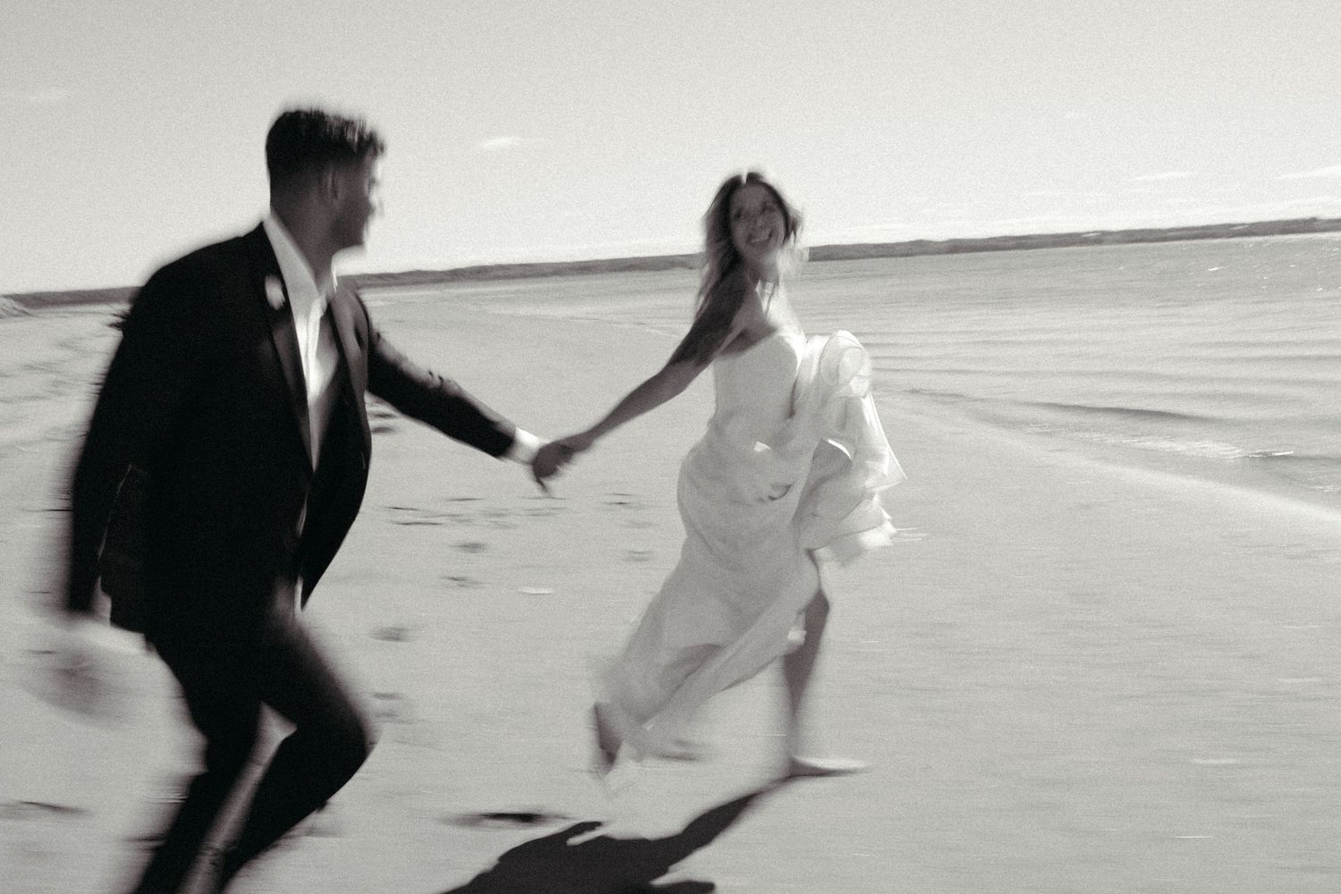 A couple walks hand-in-hand on a beach, their figures silhouetted against the horizon.