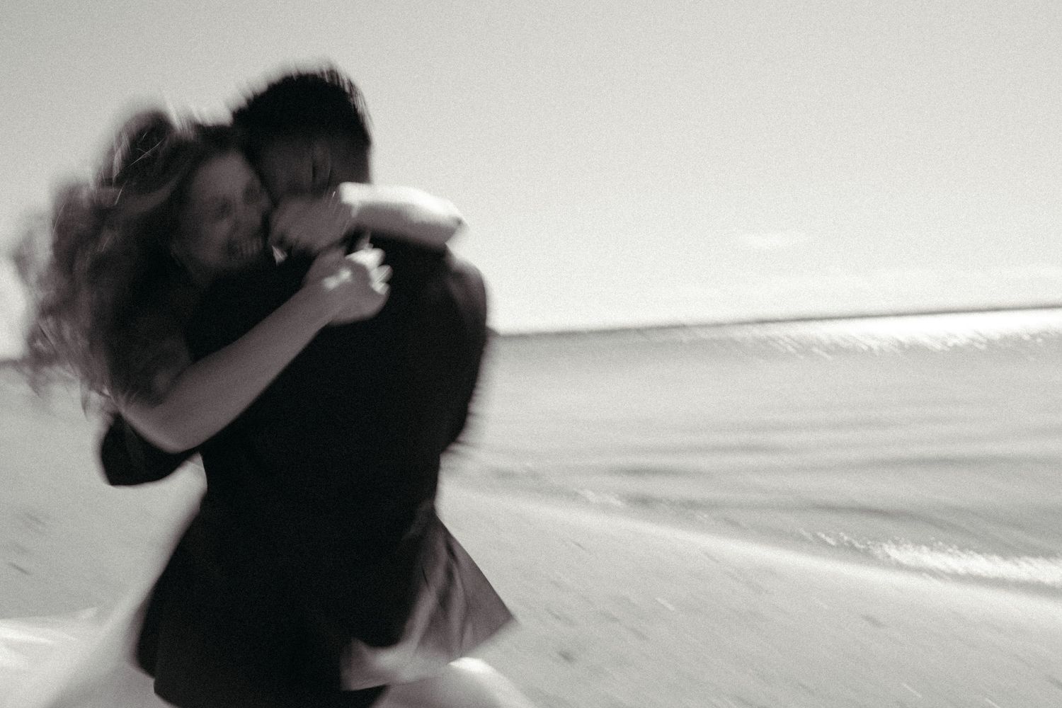 A couple embraces on a beach, captured in a black and white image.