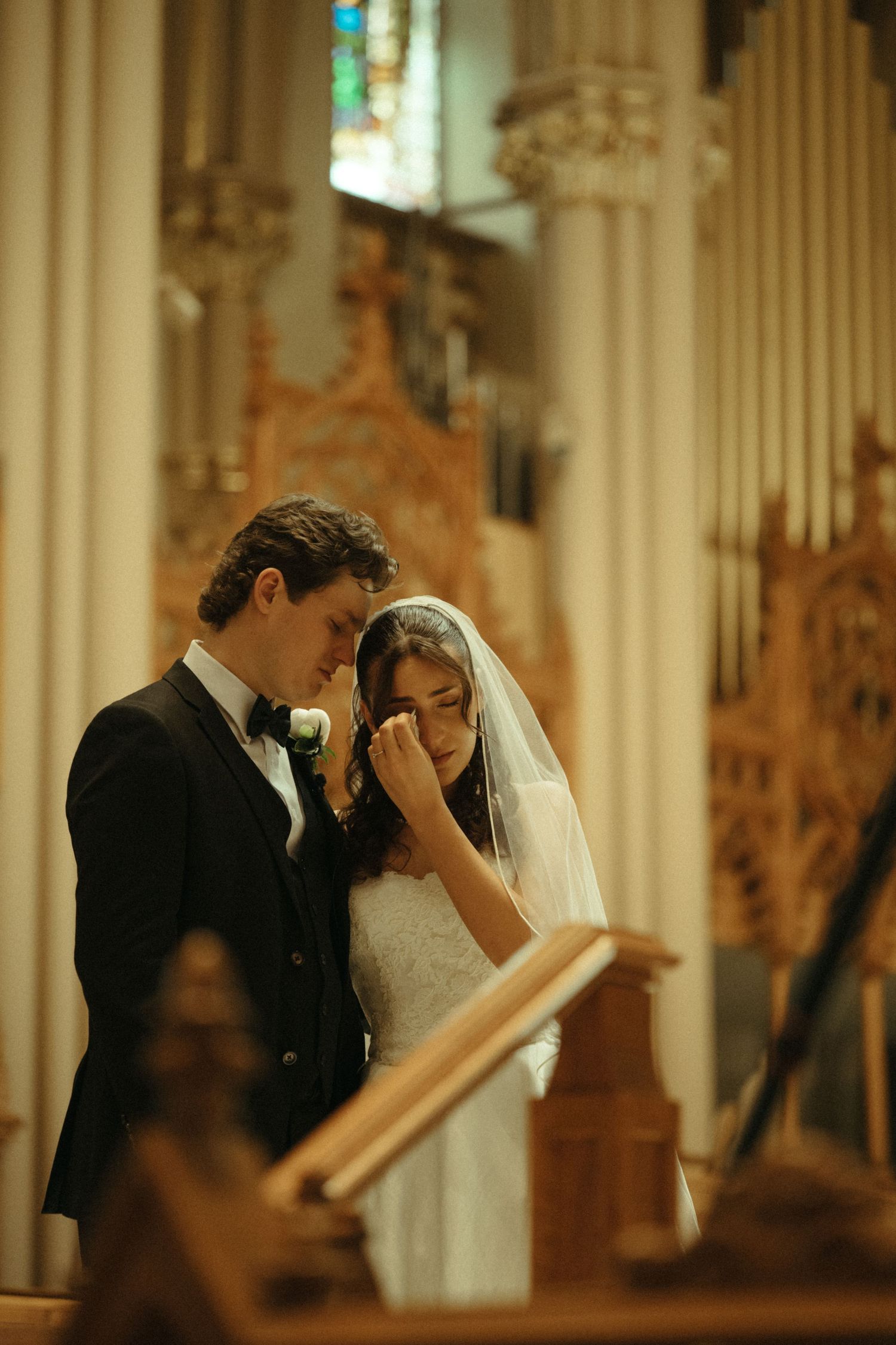 Emotional bride and groom share intimate moment at altar in ornate church during ceremony.
