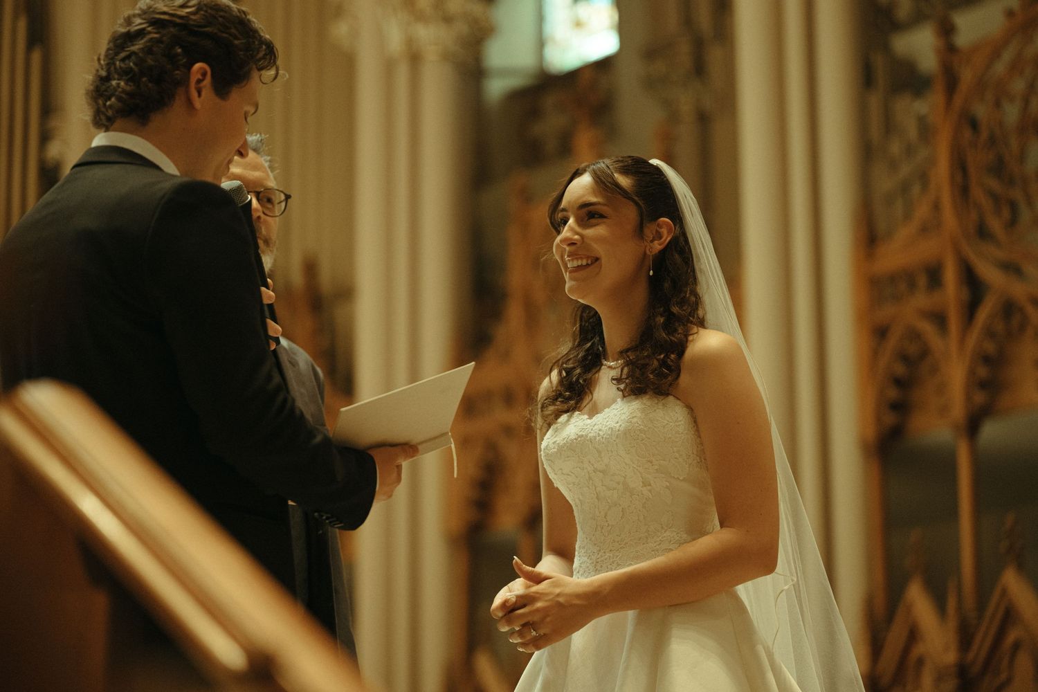 Bride and groom exchanging vows at a church altar, bride smiling in white gown during wedding ceremony.