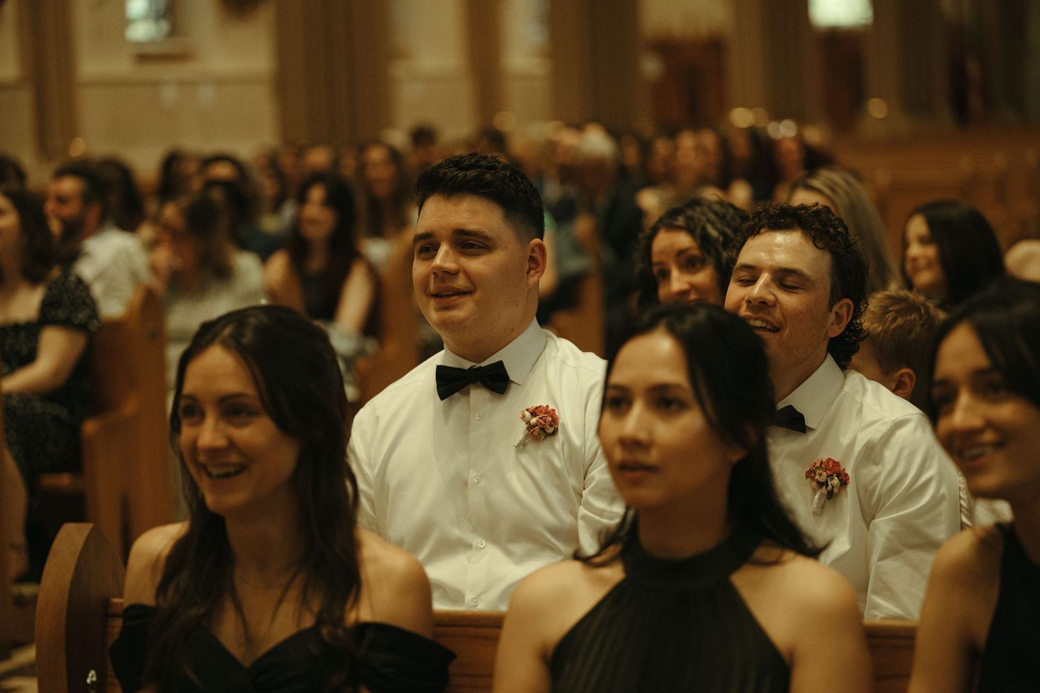 Young guests in formal attire smiling and laughing during a wedding ceremony in a grand church.