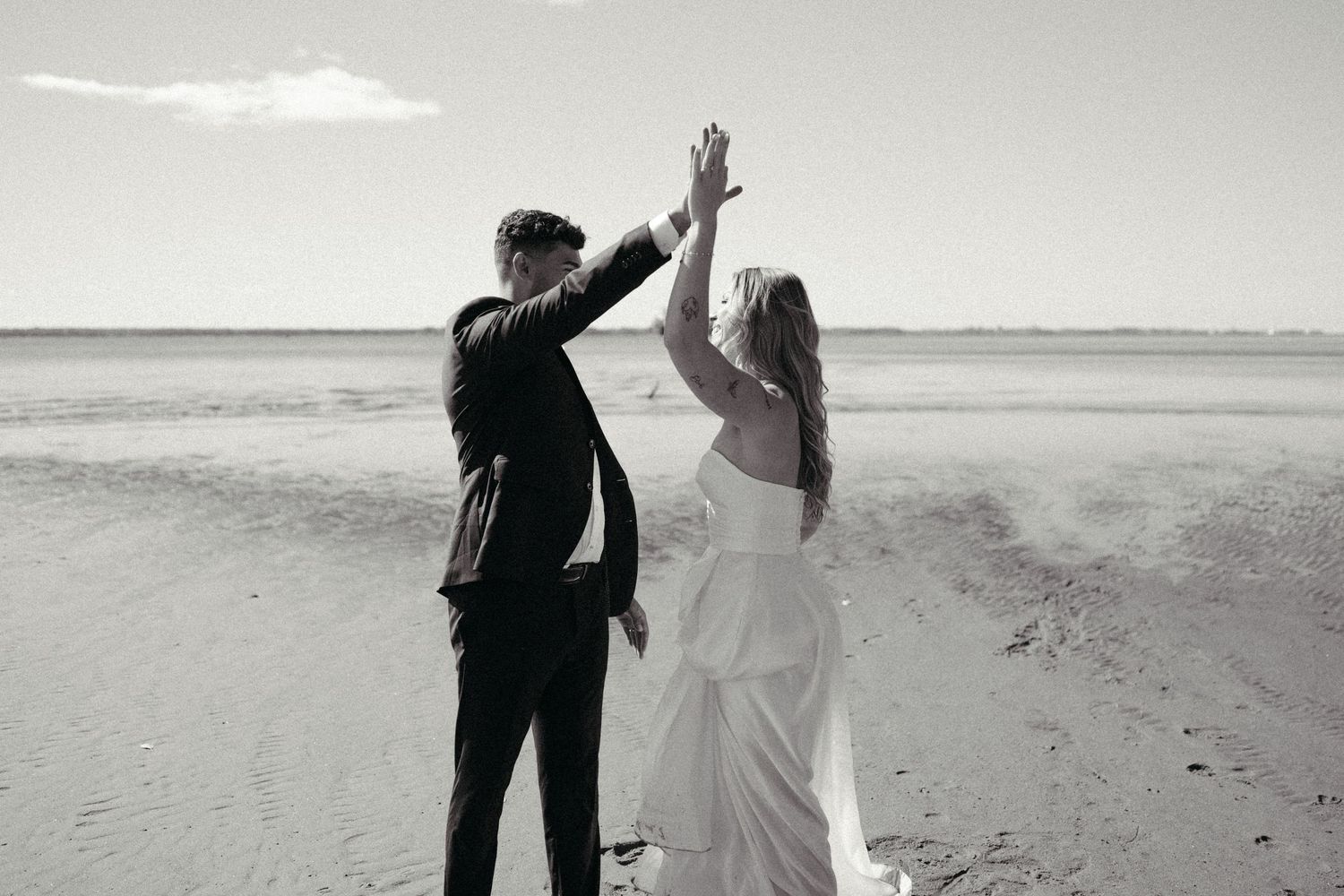 A bride and groom hold hands and walk together on a beach.