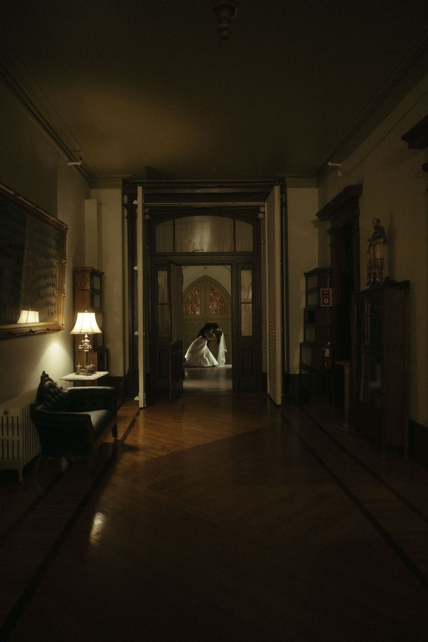 Dark moody hallway of an elegant venue with a glowing lamp and silhouette of a couple in the doorway.