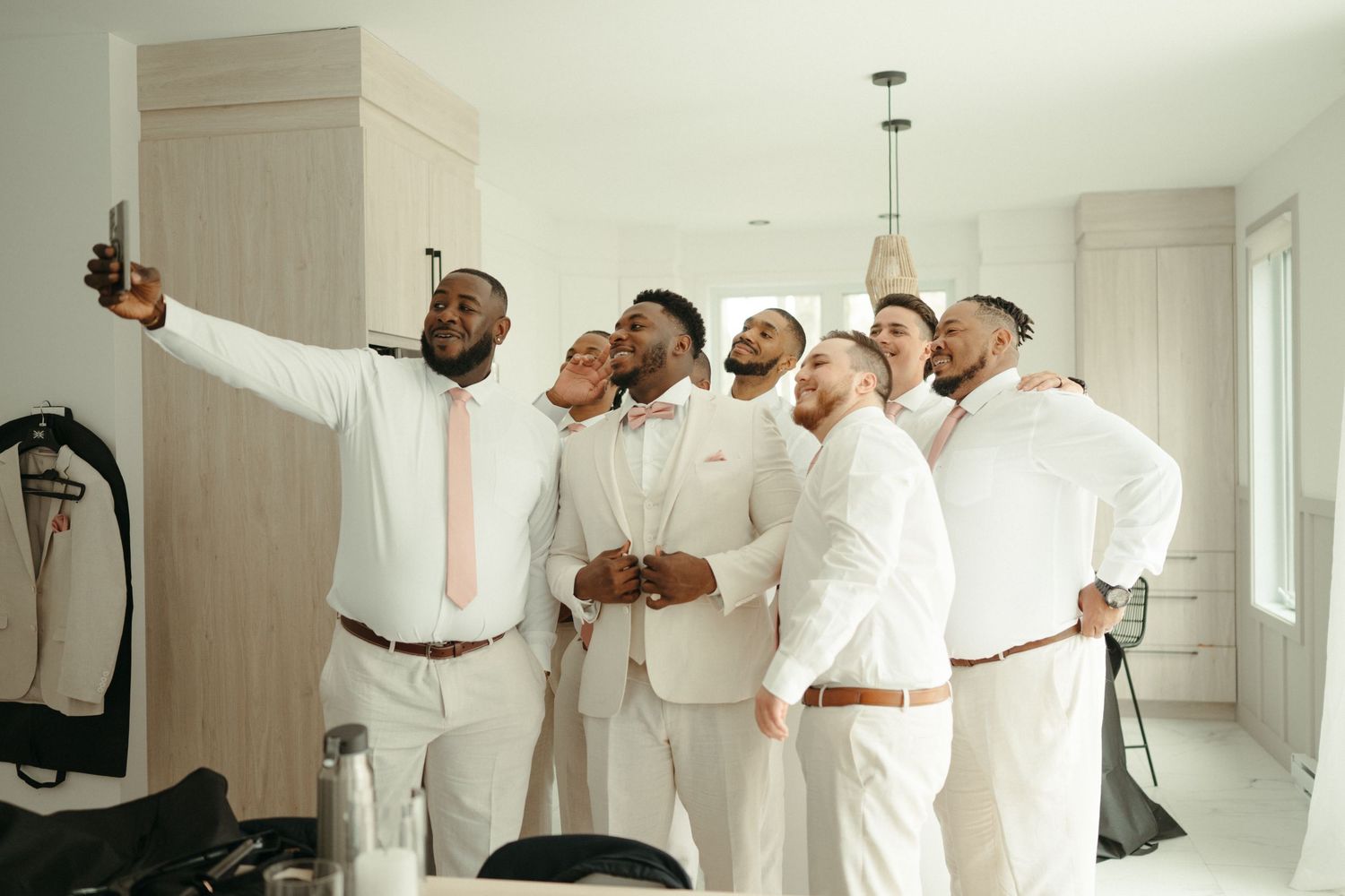 Groom and groomsmen in white suits take a fun selfie together before the wedding ceremony.