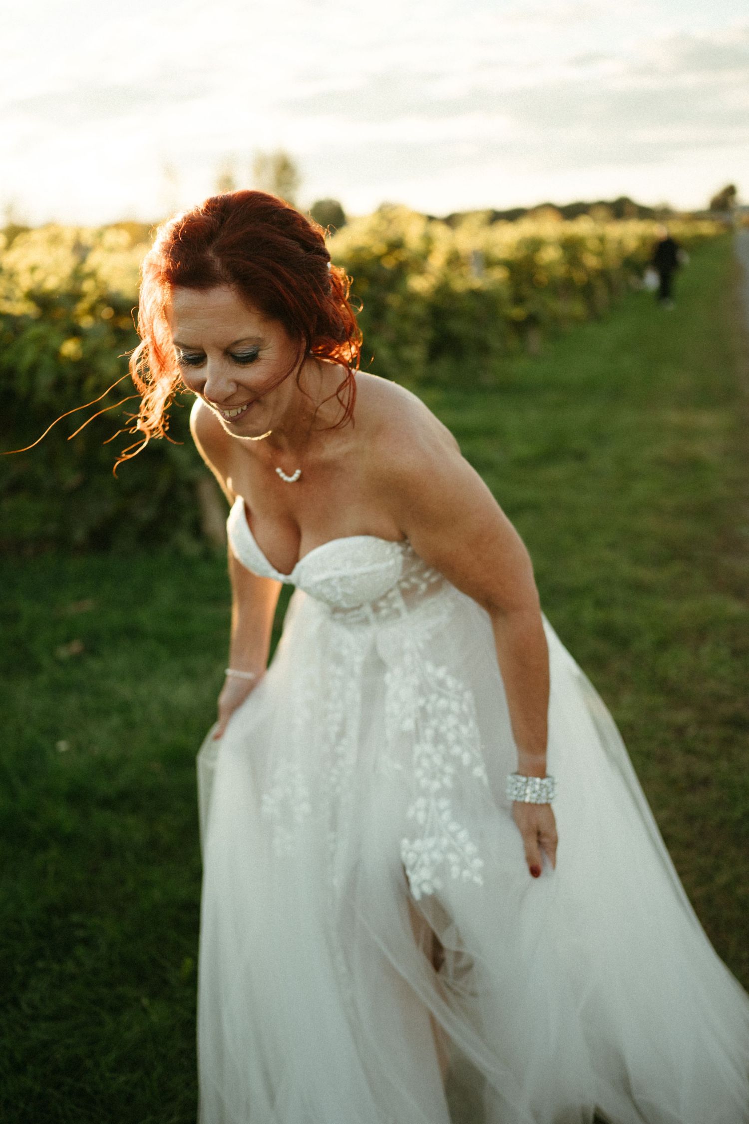 Bride in white tulle gown twirling in vineyard at golden hour sunset.