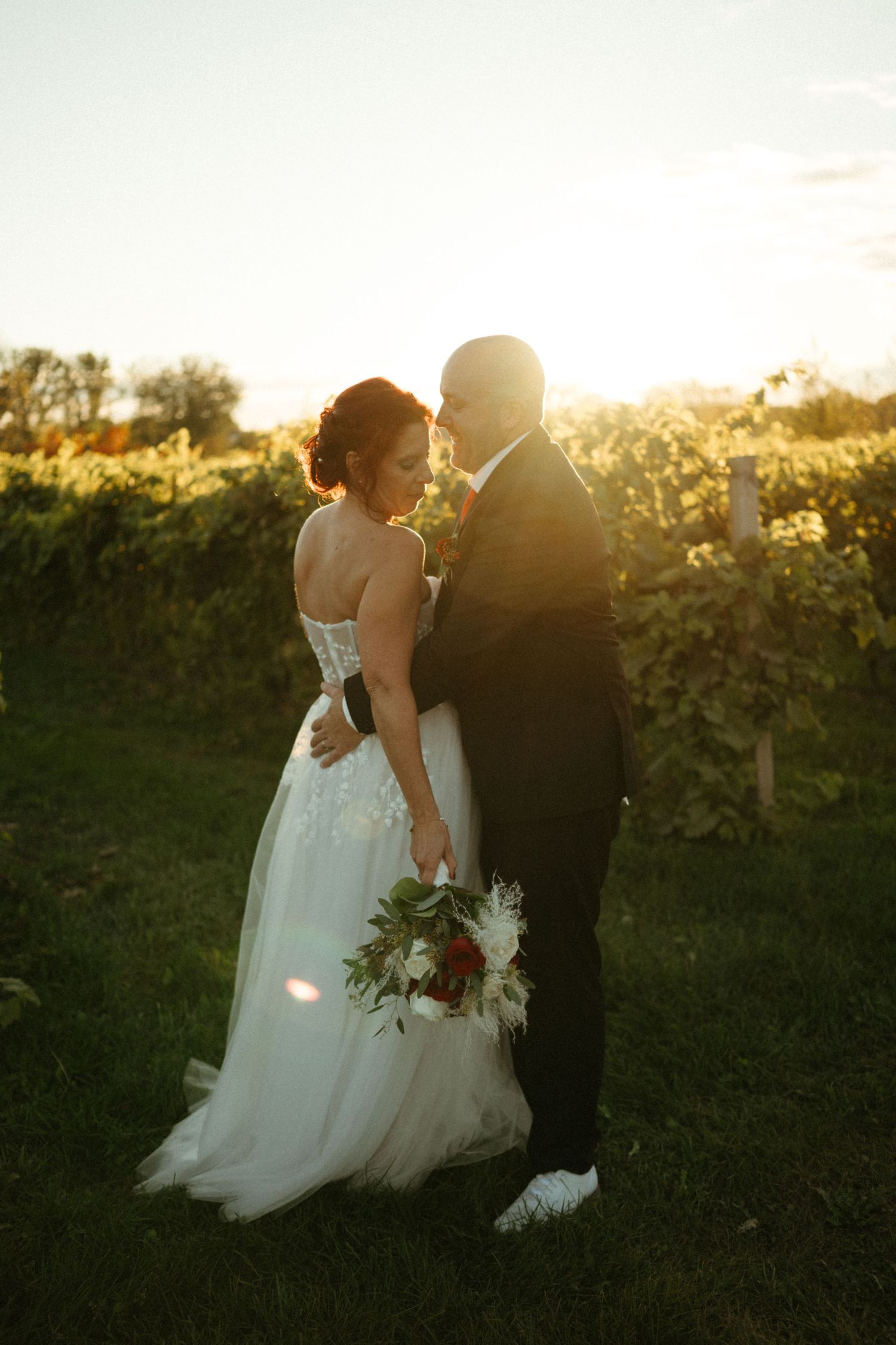 Bride and groom sharing romantic moment in vineyard at glowing sunset.