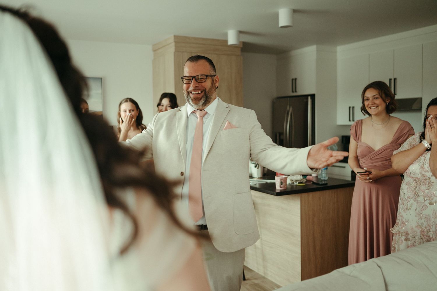 Groom in beige suit reacts with joy seeing bride for first time at wedding first look reveal.