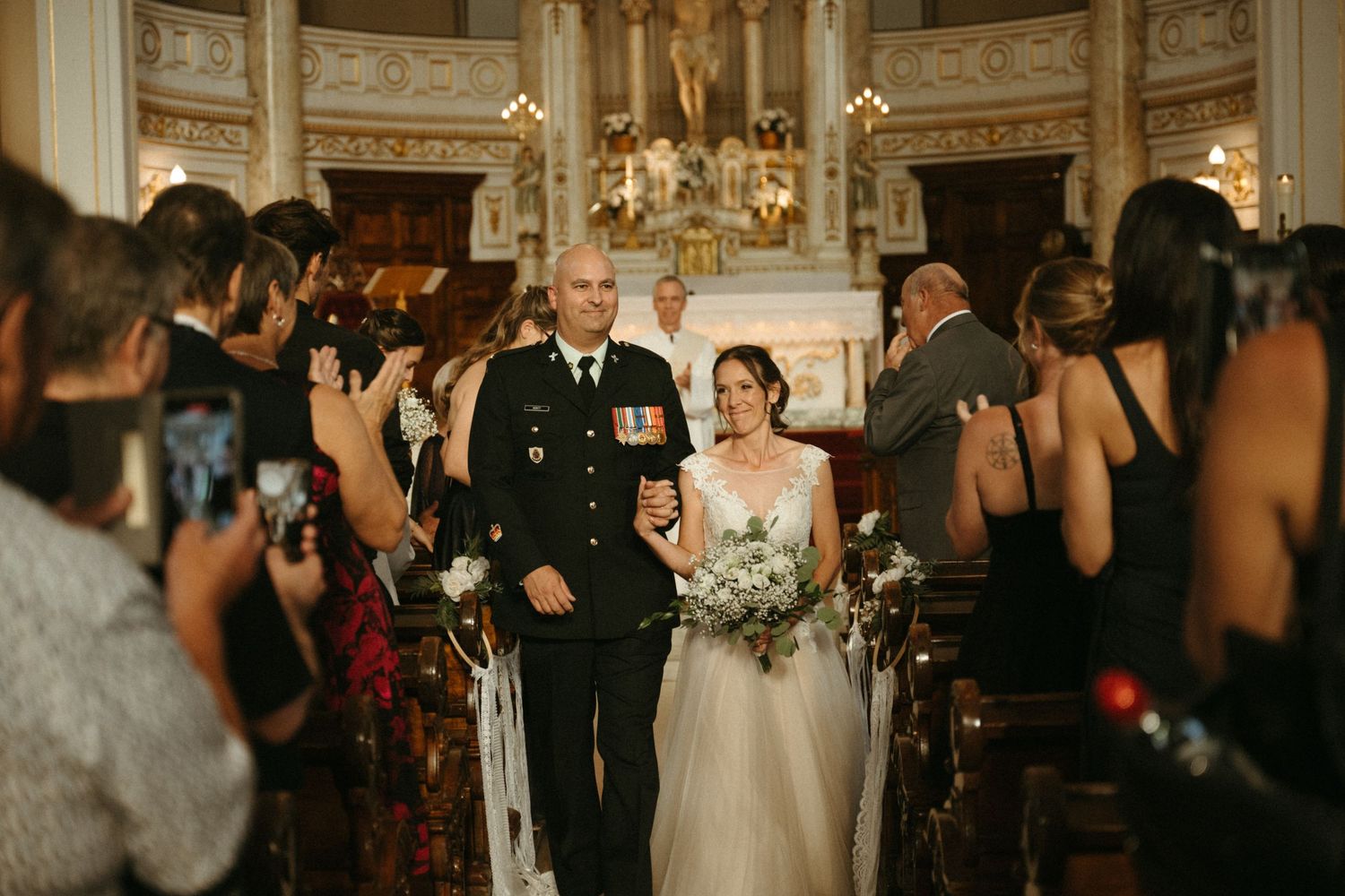 Military groom in dress uniform walks bride in white lace gown down church aisle after ceremony.
