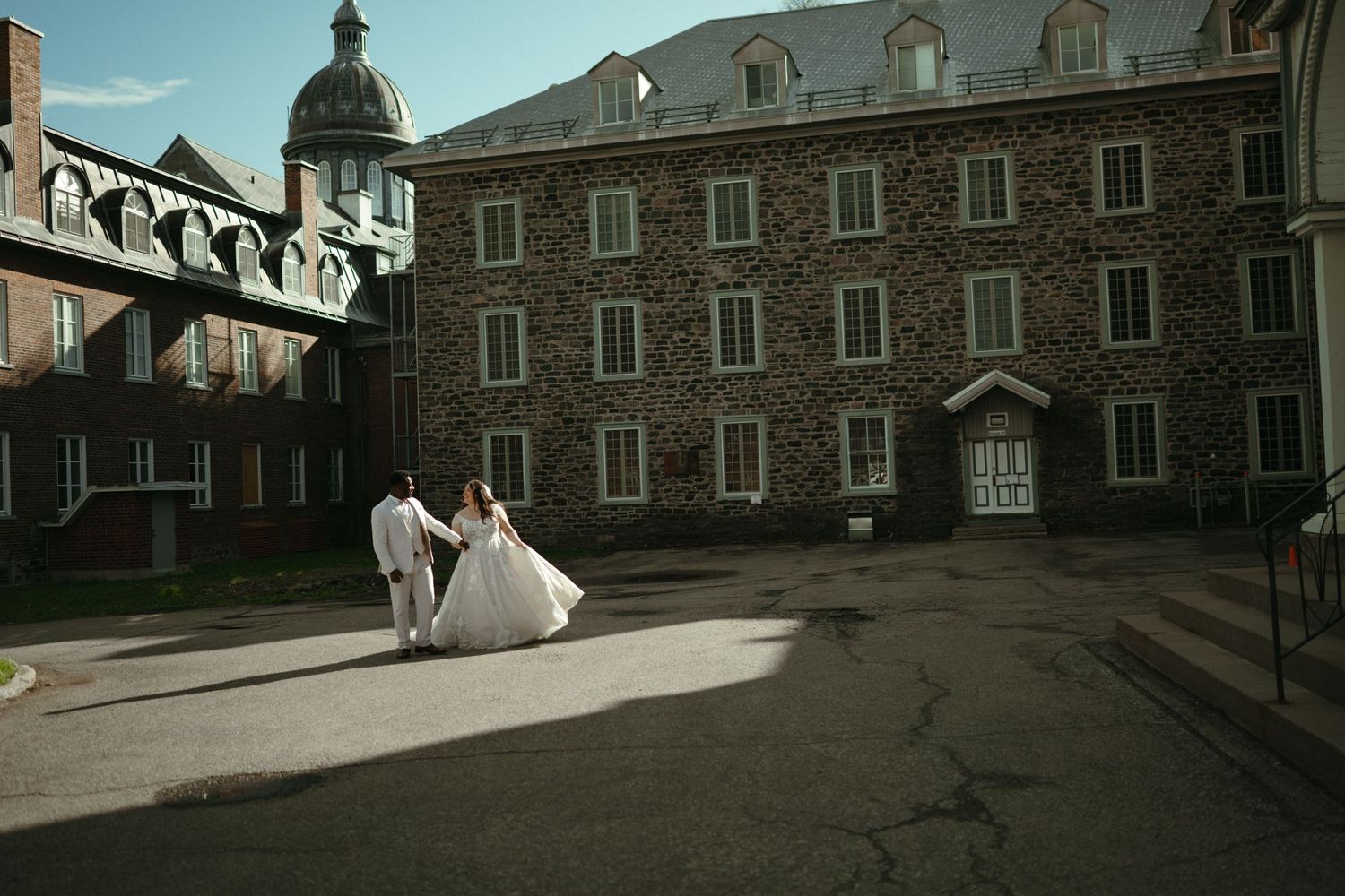 Bride and groom walking hand in hand outside a grand historic stone building.