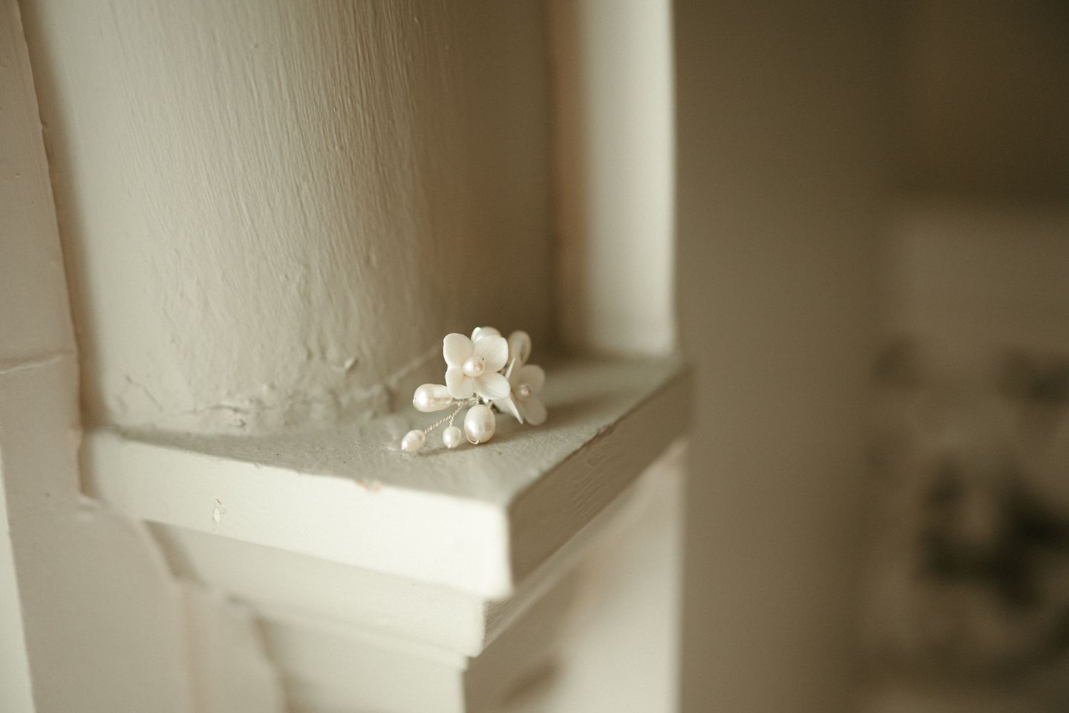 Delicate white floral hair accessory with pearl details resting on white painted wooden mantelpiece ledge.
