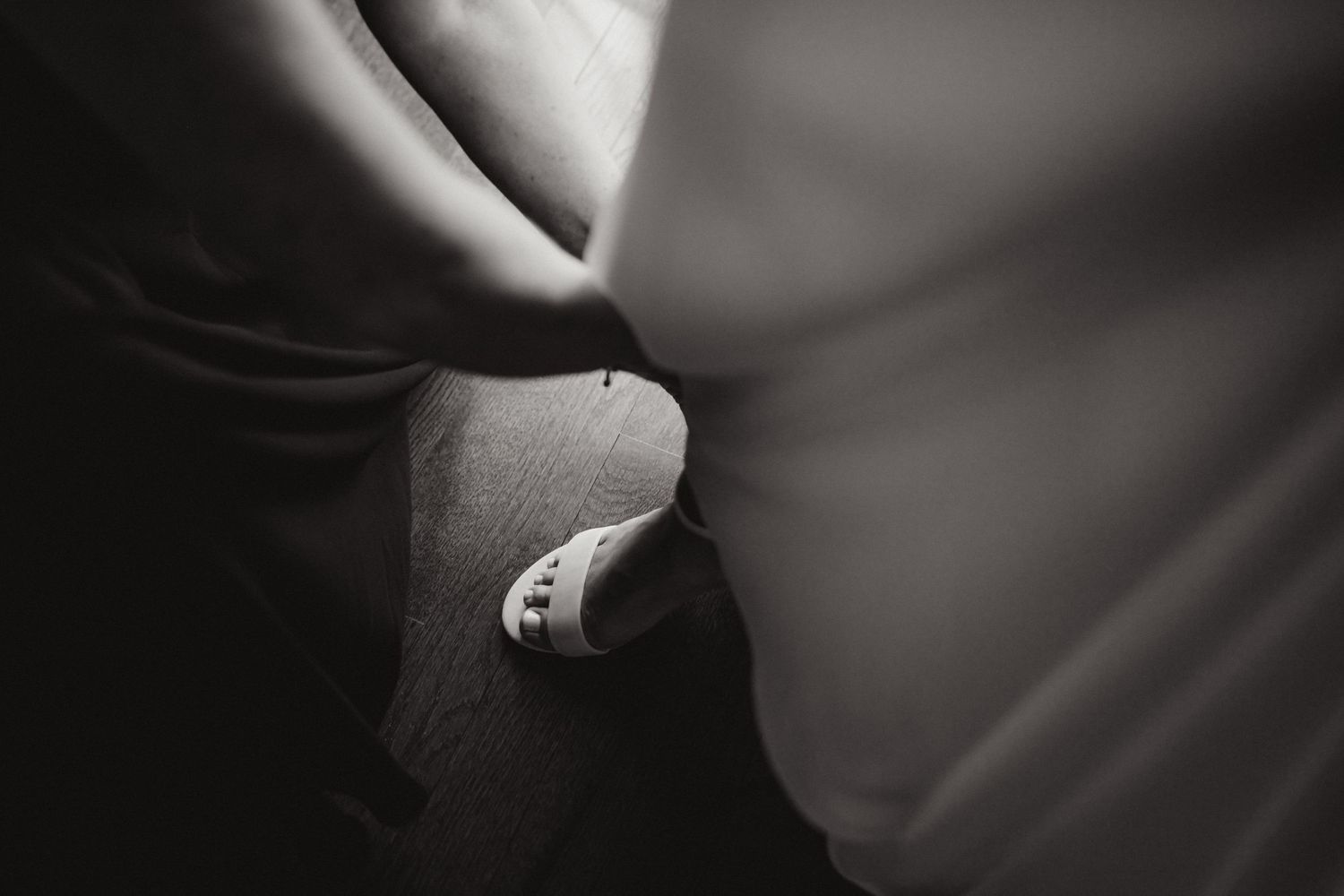 Close-up black and white photo of a pregnant belly with a tiny baby shoe resting against it.