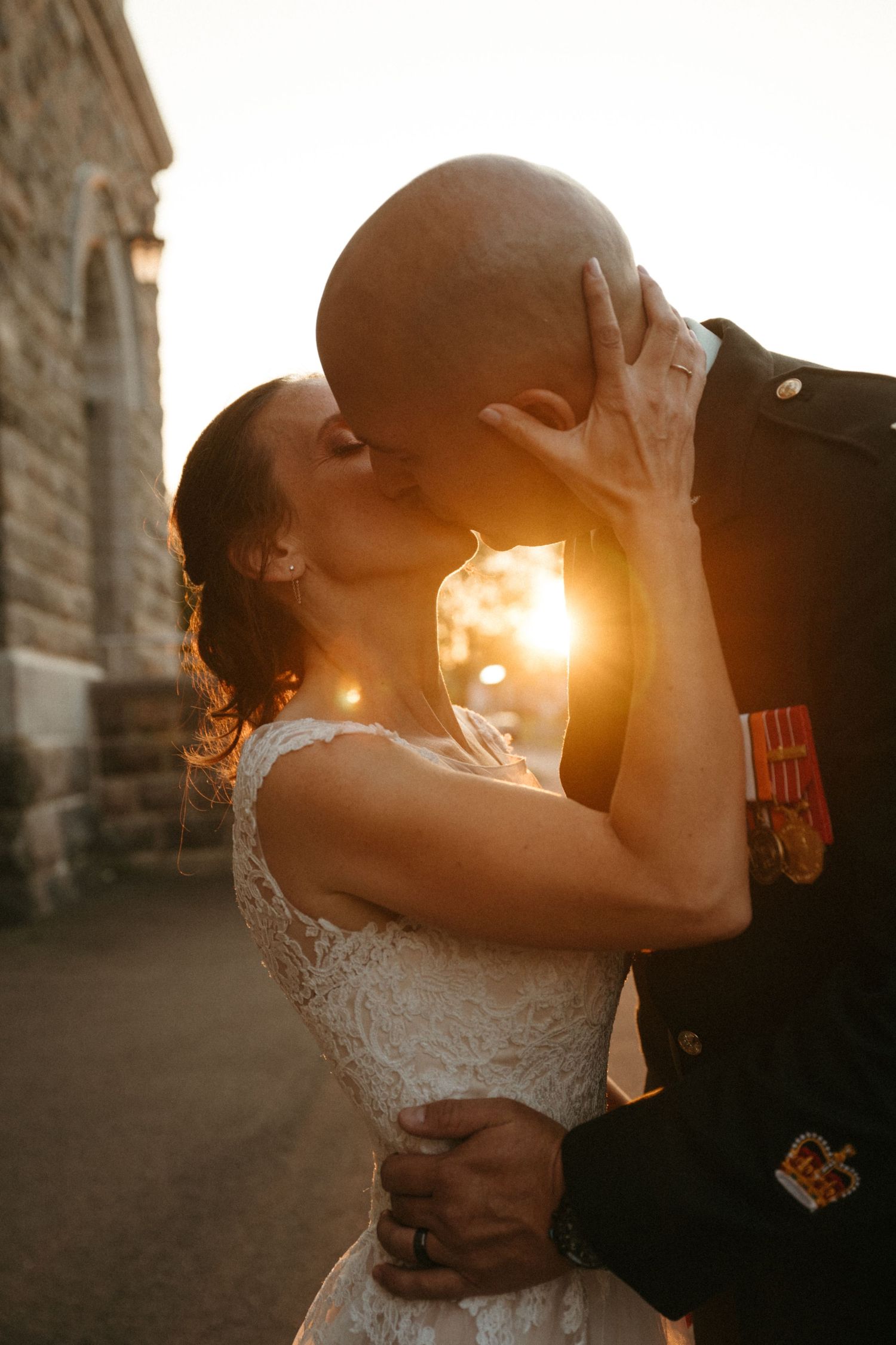Bride and groom share a romantic sunset kiss, groom wearing military uniform with medals.
