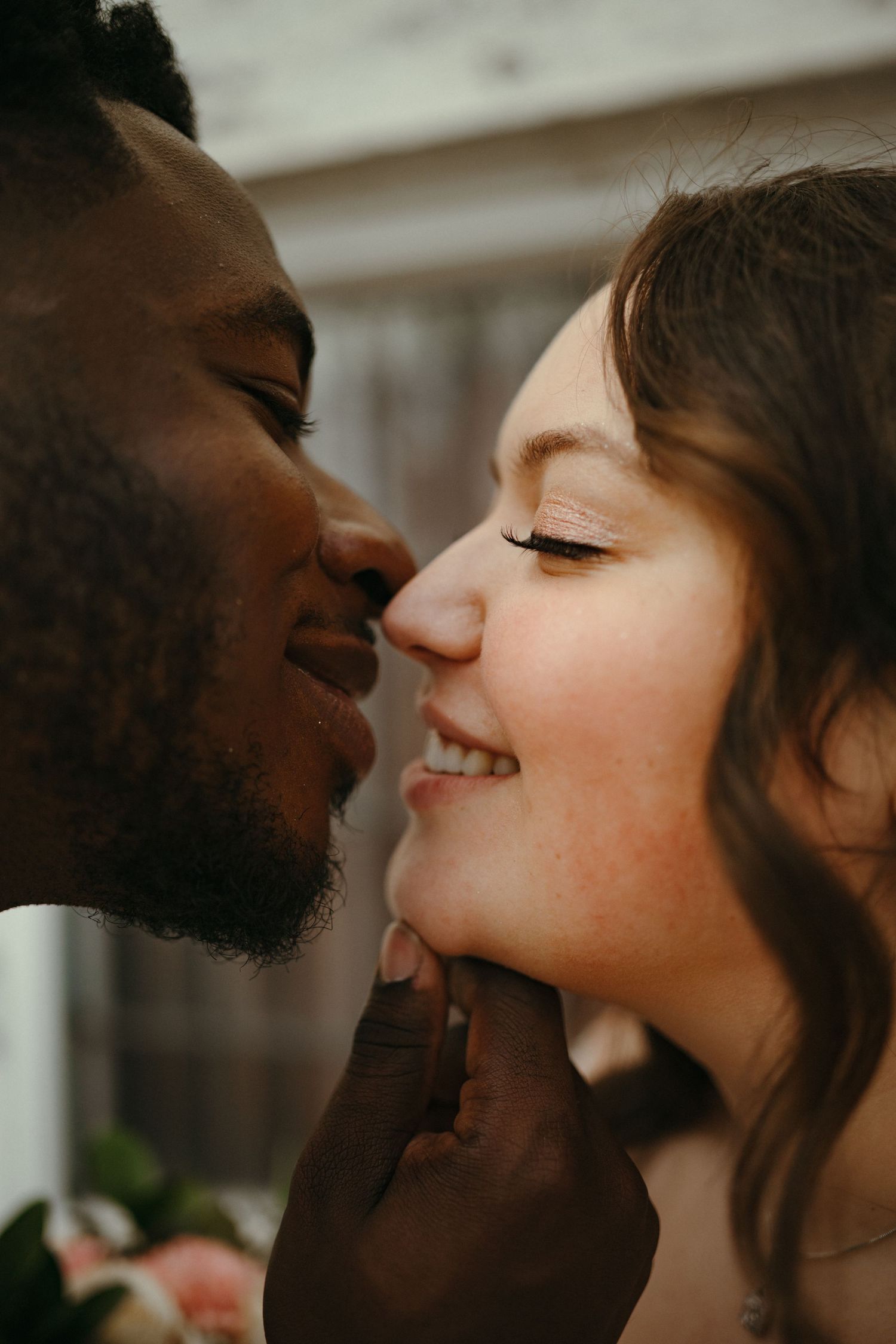 Interracial couple sharing a romantic moment, smiling and almost kissing, bride wearing natural makeup.
