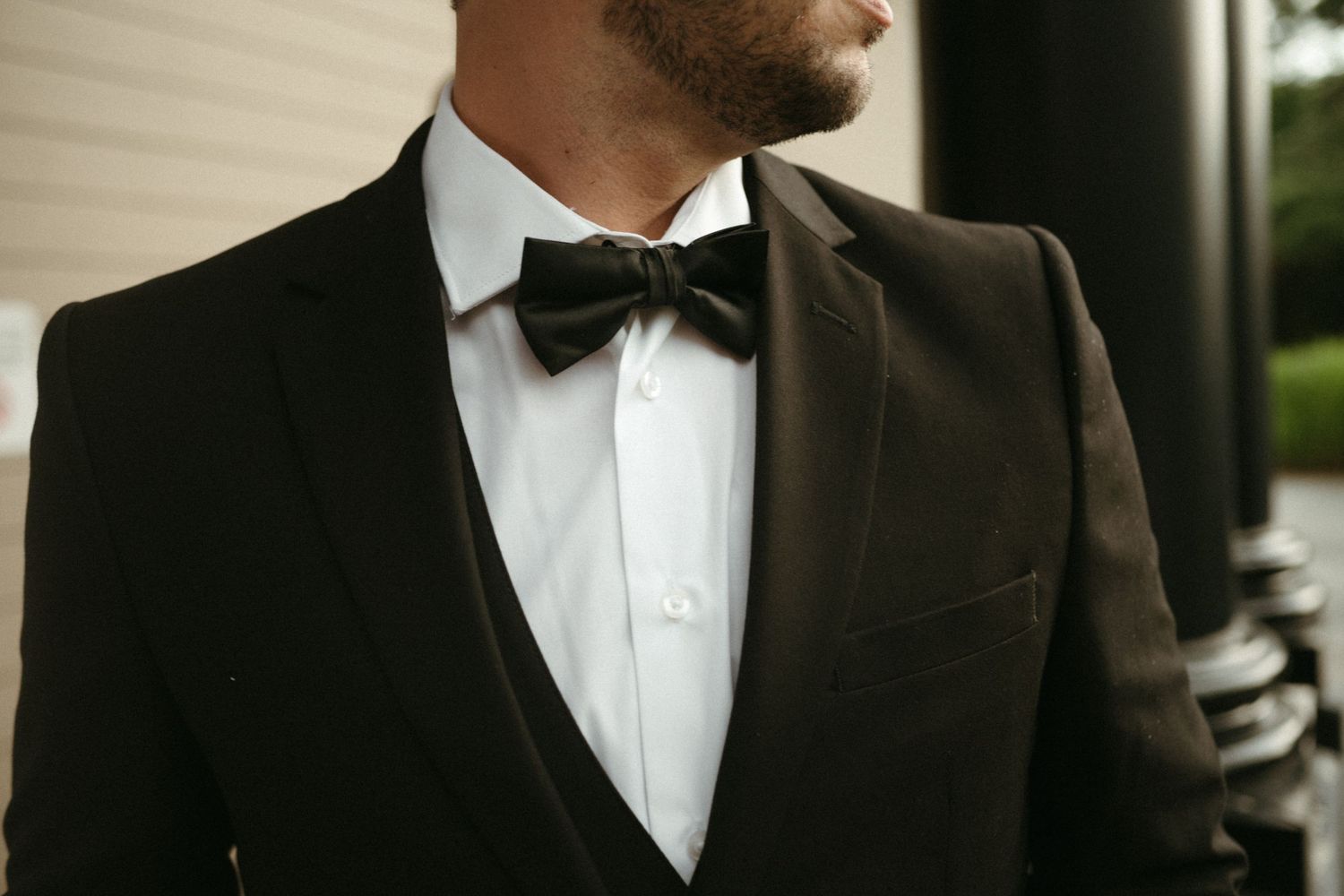 Close-up of groom in black tuxedo with bow tie and white dress shirt at wedding.