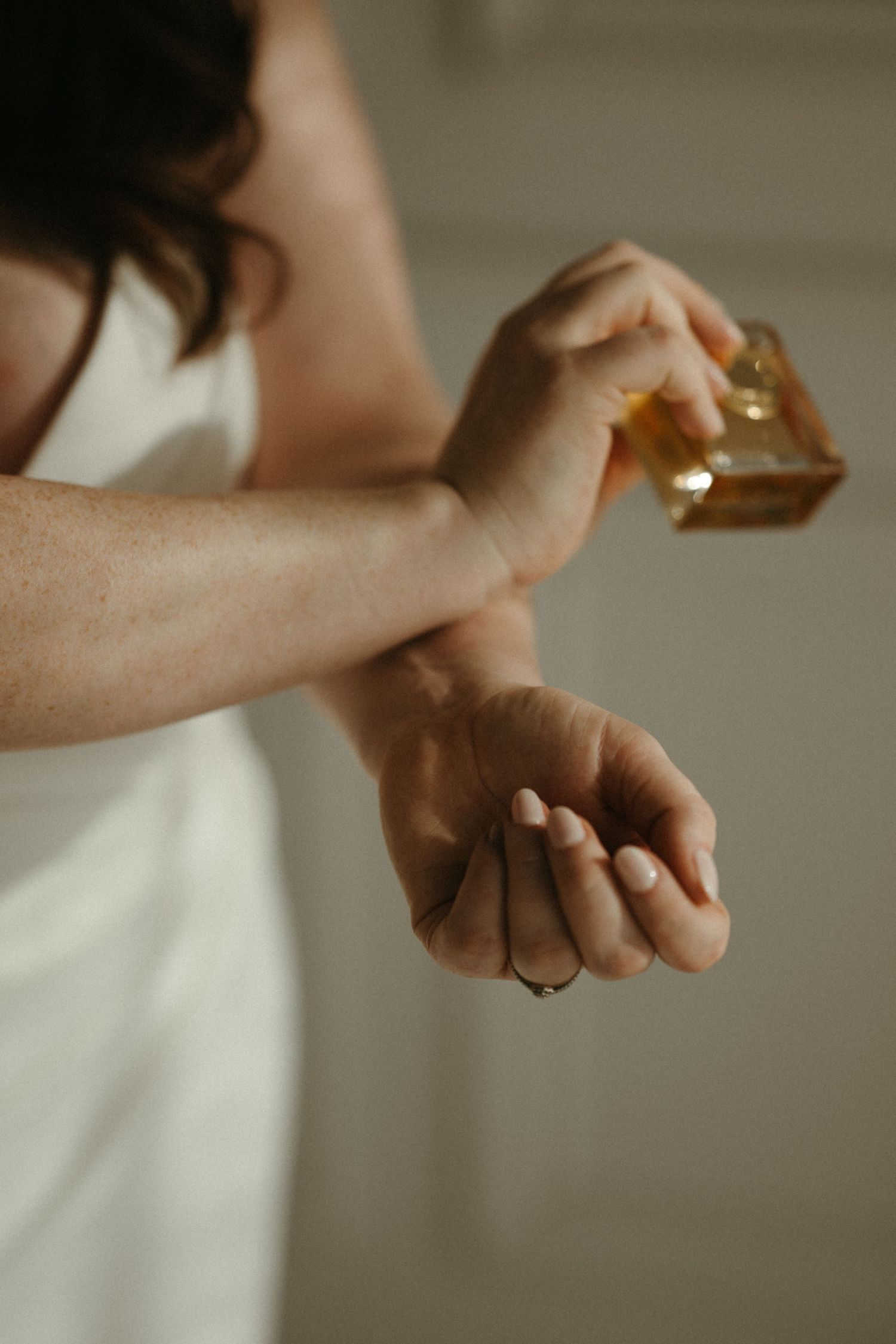 Bride applies perfume to her wrist wearing a white dress, with a gold fragrance bottle.