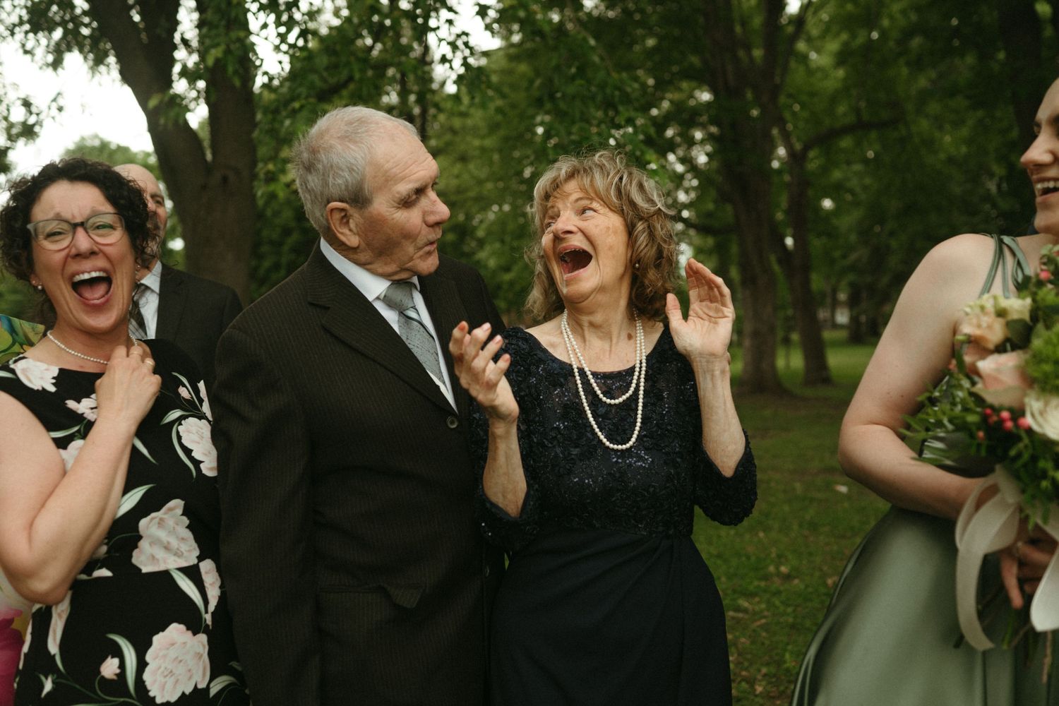 Joyful family group laughing together outdoors at a wedding celebration, dressed in formal attire.