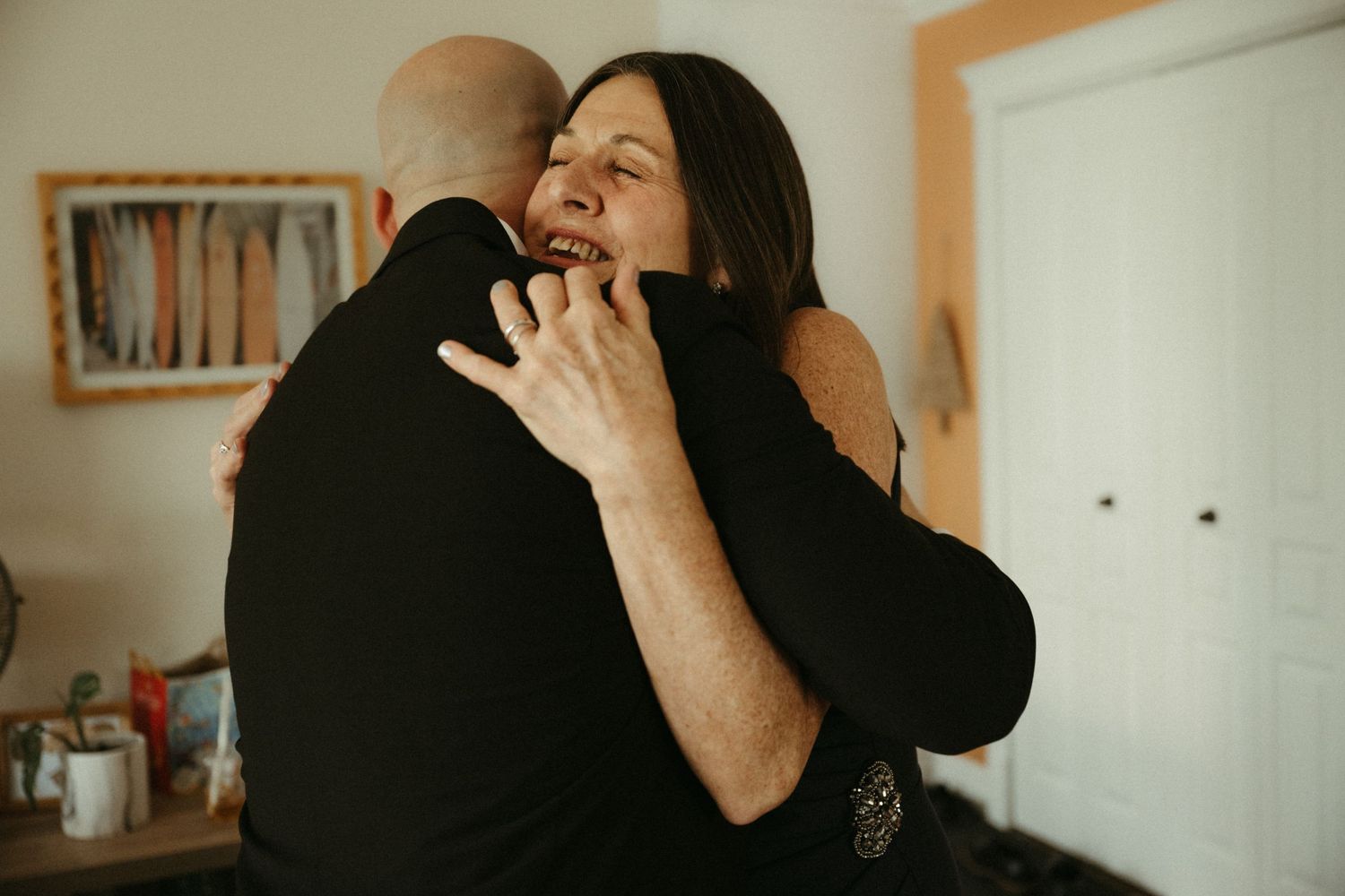 Emotional mother and son sharing a heartfelt hug indoors on wedding day.