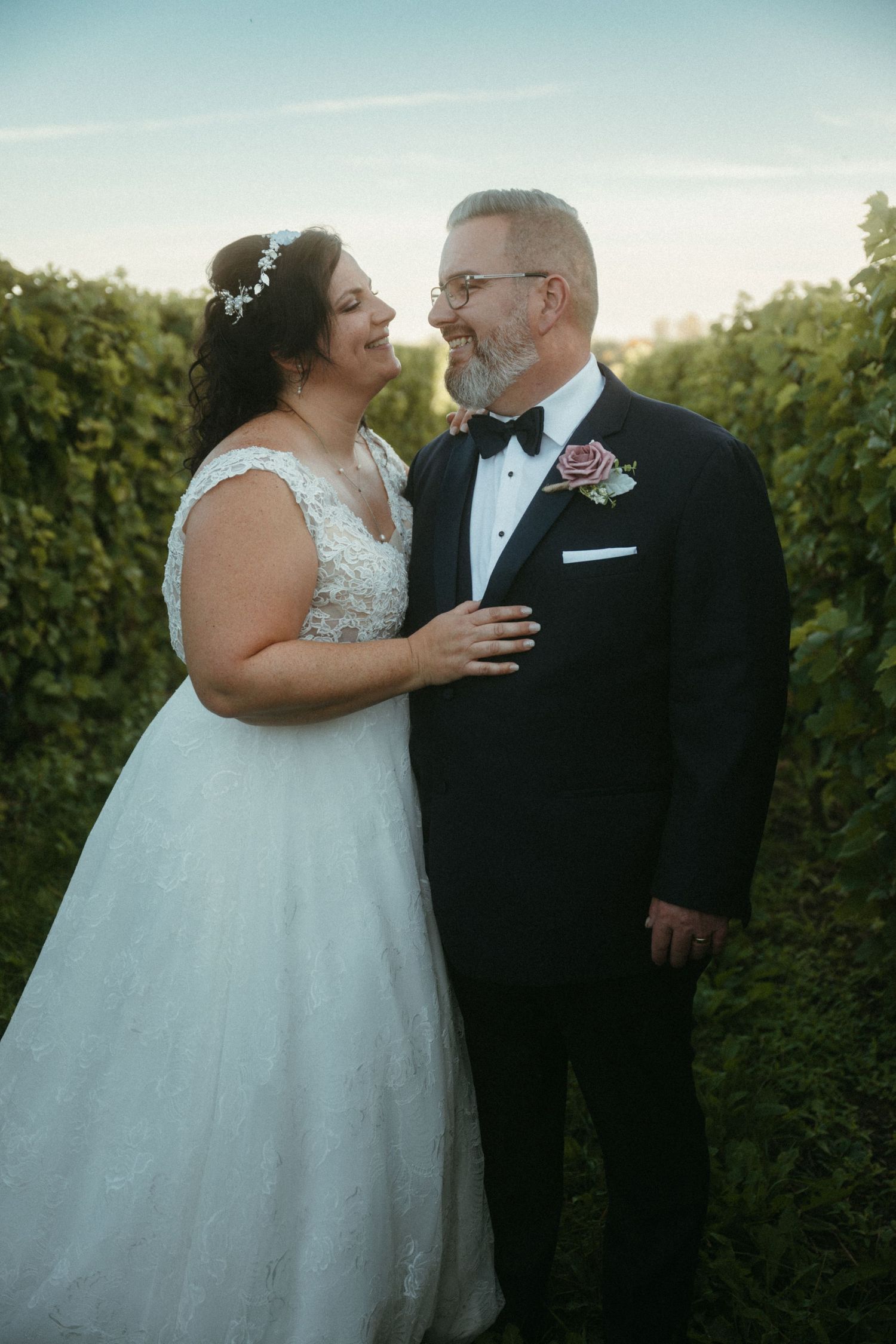 Bride and groom share a joyful moment together in a lush vineyard at golden hour.
