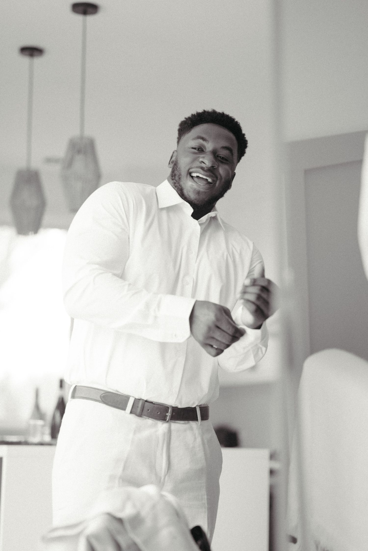 Happy groom in white shirt laughing and dancing during wedding preparations in black and white photo.