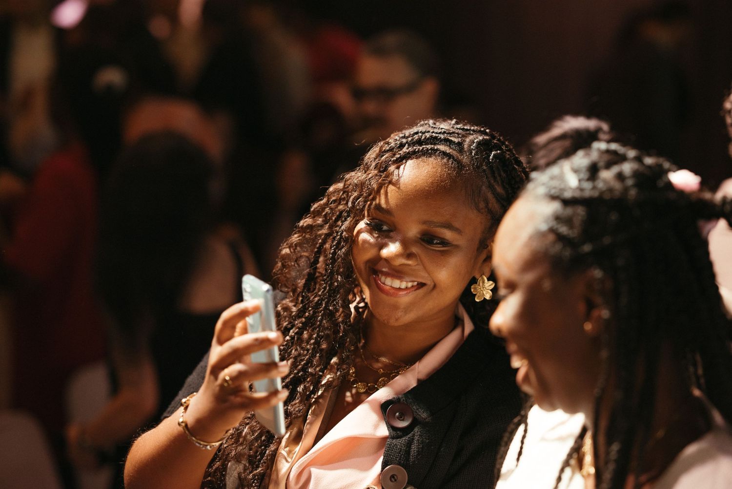 Two women smiling and laughing together at a warmly lit wedding reception celebration.