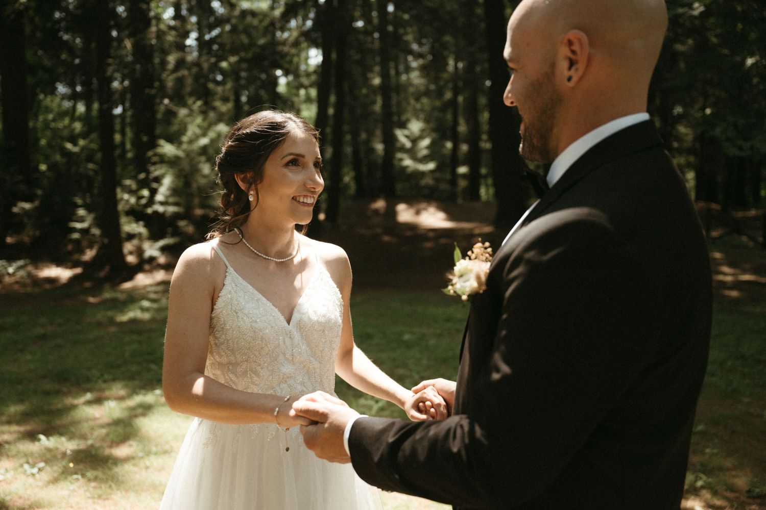 Bride and groom sharing an emotional first look moment while holding hands in a sunlit forest.