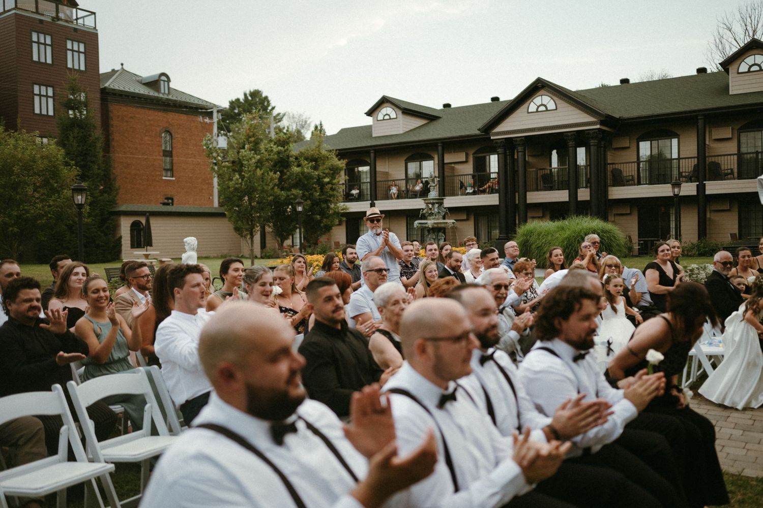 Wedding guests applaud and celebrate during an outdoor ceremony at a historic brick venue.