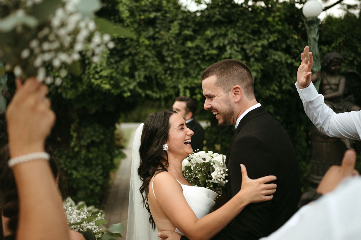 Bride and groom laugh joyfully together during their outdoor wedding ceremony surrounded by guests.