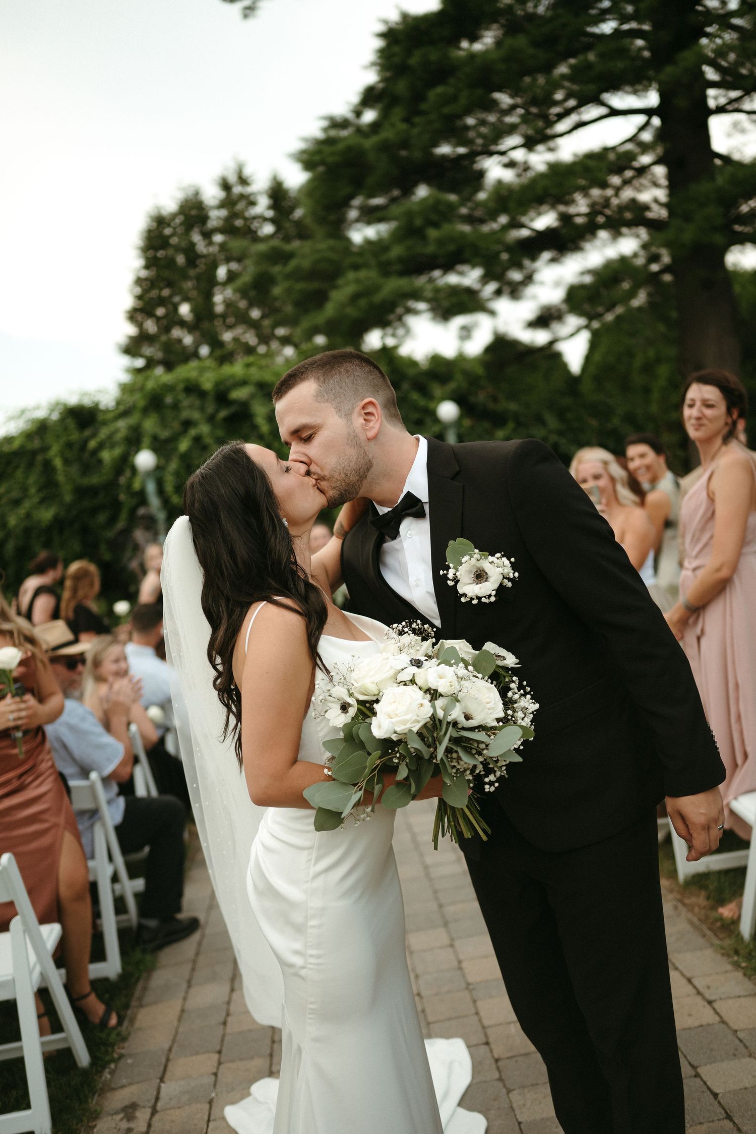 Bride and groom share a first kiss while walking down the aisle at an outdoor wedding ceremony.