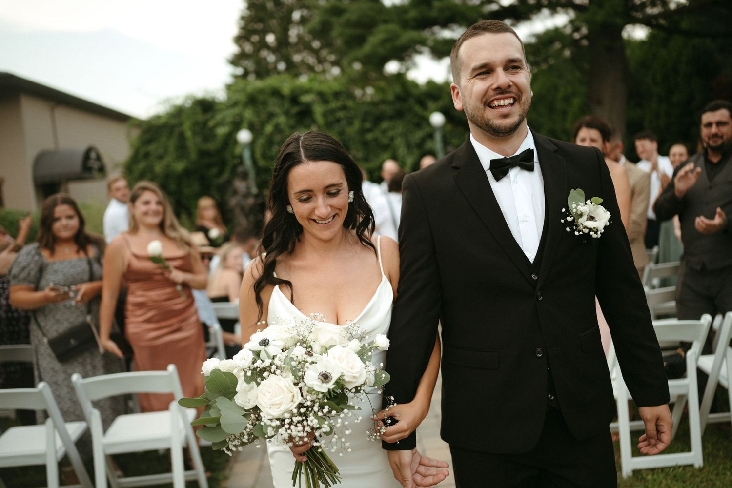 Smiling newlyweds walk back down the aisle hand in hand after their outdoor wedding ceremony.