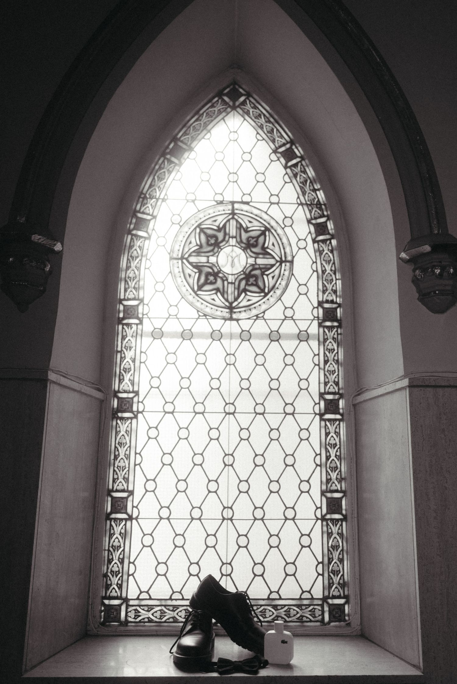Black and white photo of dress shoes beside stained glass church window on wedding day.