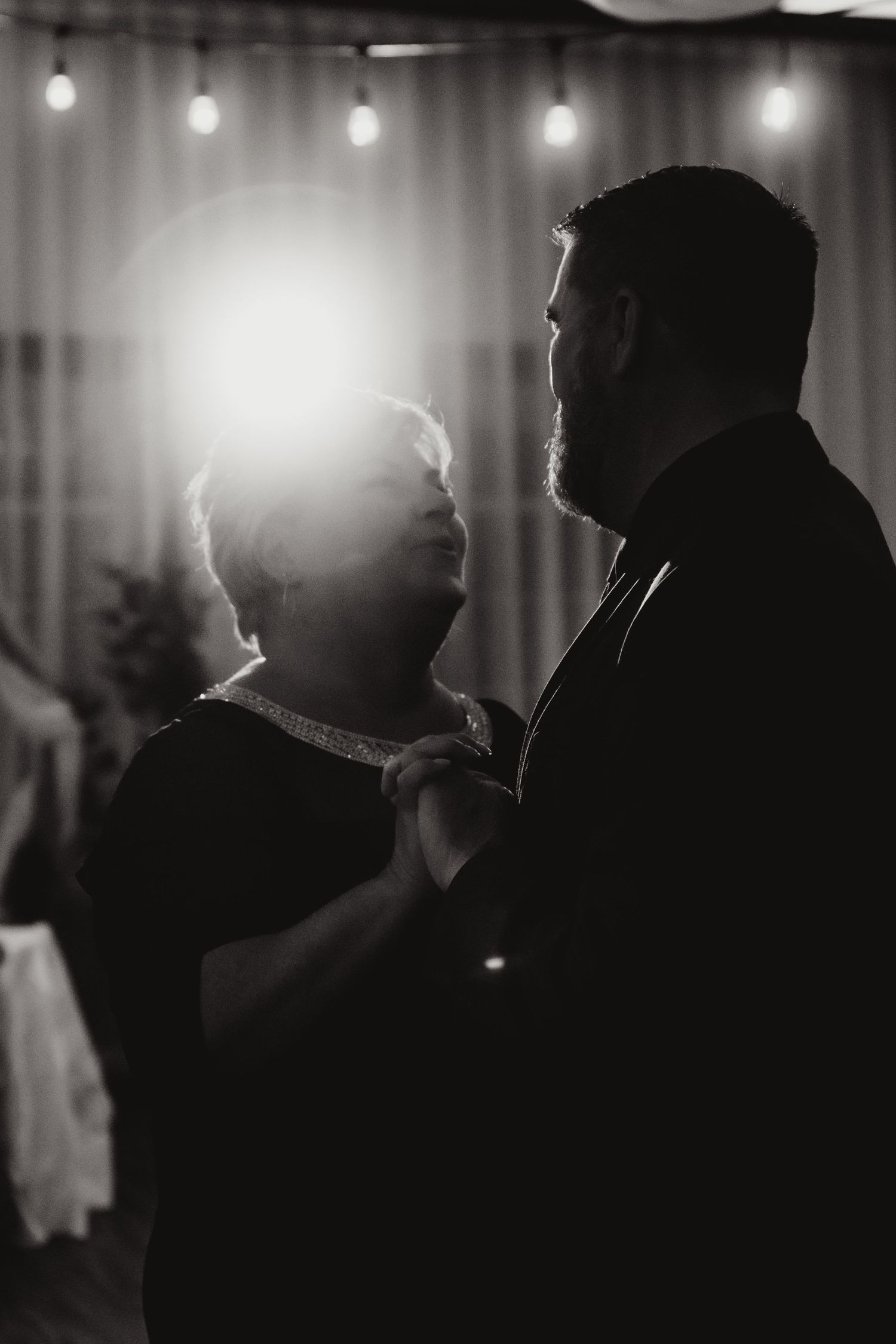 Black and white photo of a groom and his mother sharing an emotional dance at a wedding reception.