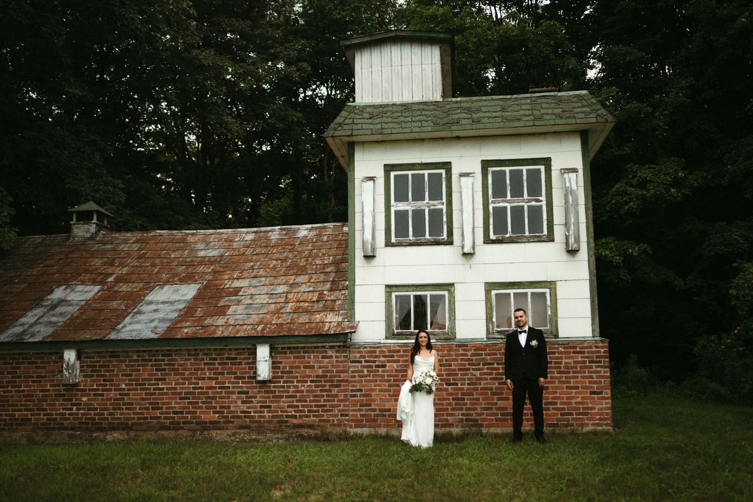 Bride and groom standing apart in front of rustic brick and white wedding venue building.