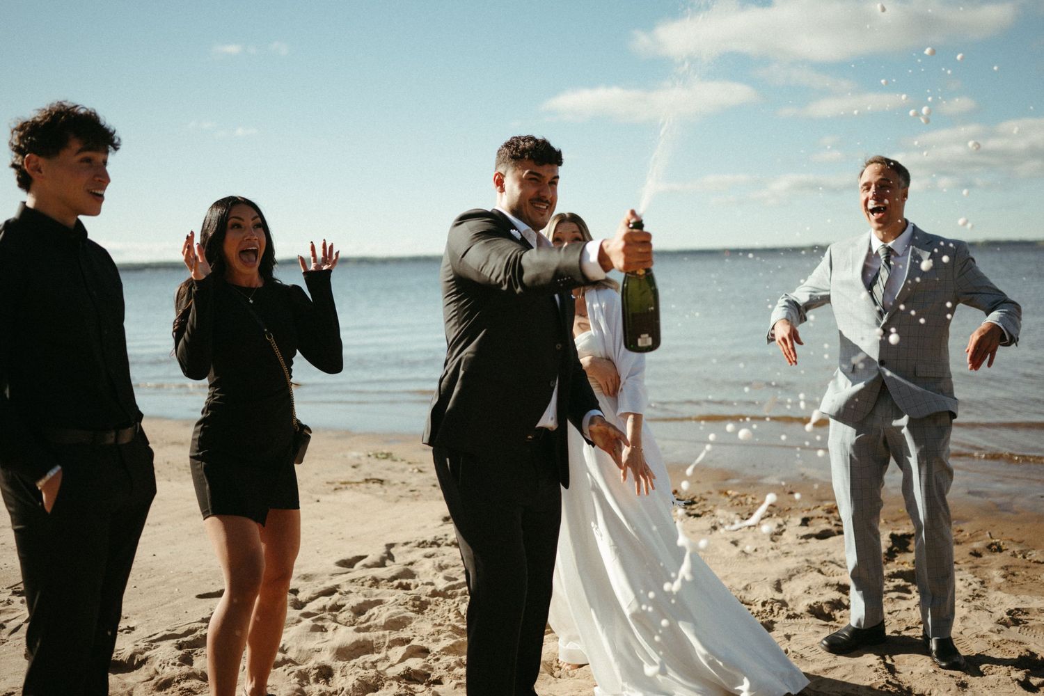 A group of people, including a bride in a white dress, standing on a beach.