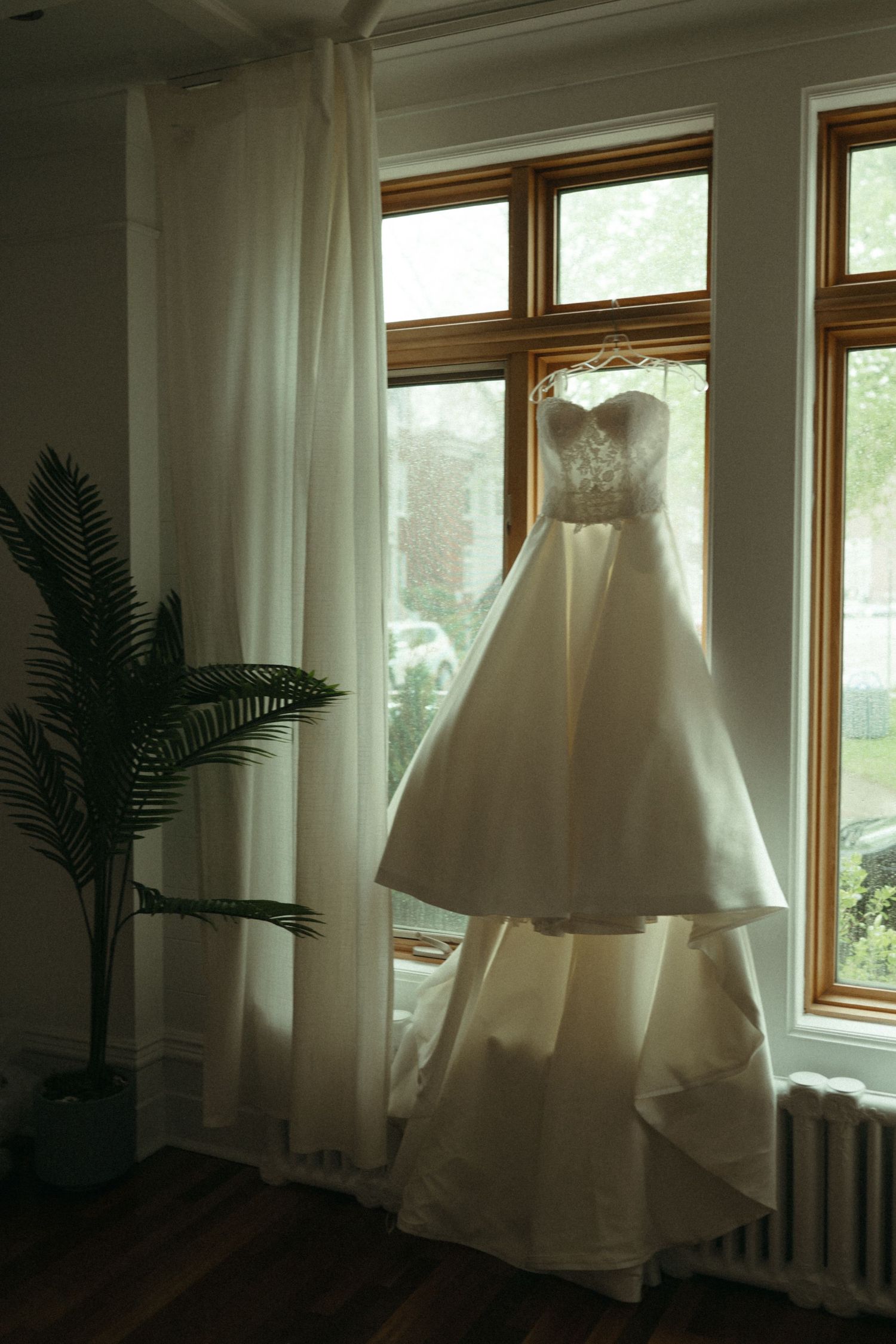 Elegant strapless white wedding ball gown hanging in window with layered skirt and beaded bodice detail.