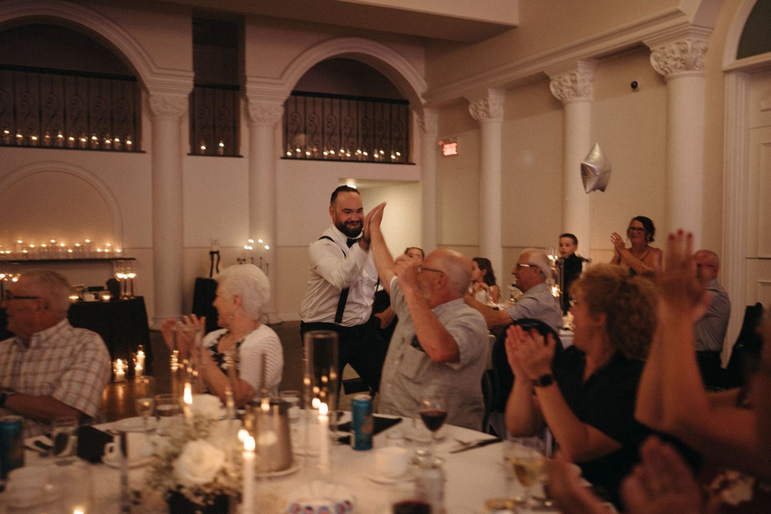 Wedding guest stands and applauds during reception speech in an elegant candlelit ballroom.