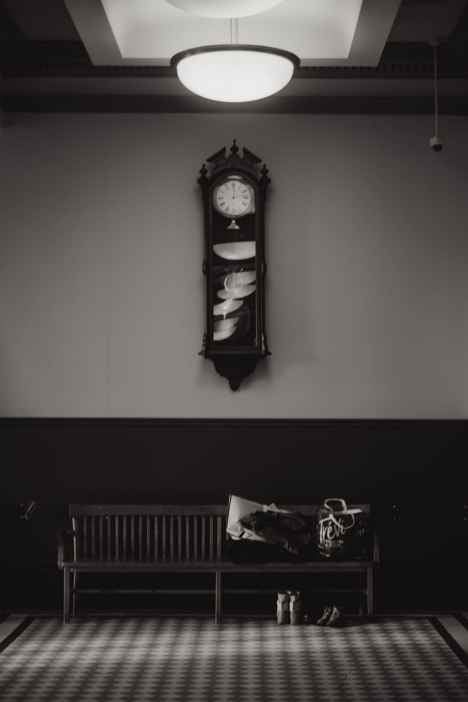 Black and white photo of vintage grandfather clock above wooden bench in elegant wedding venue.