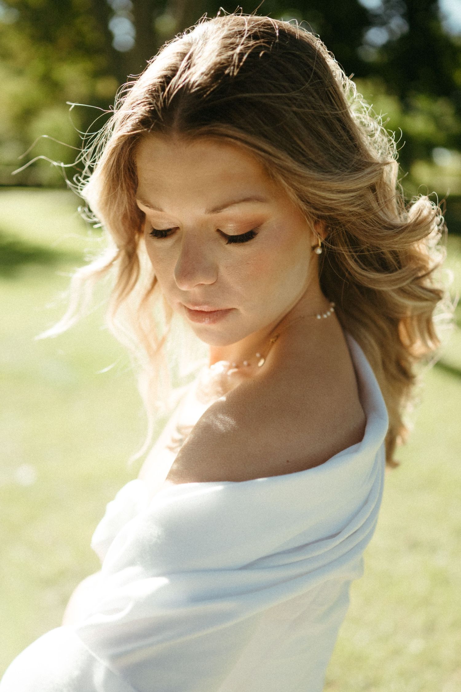 A young woman with long, wavy blonde hair and a serene expression, standing in a grassy field.