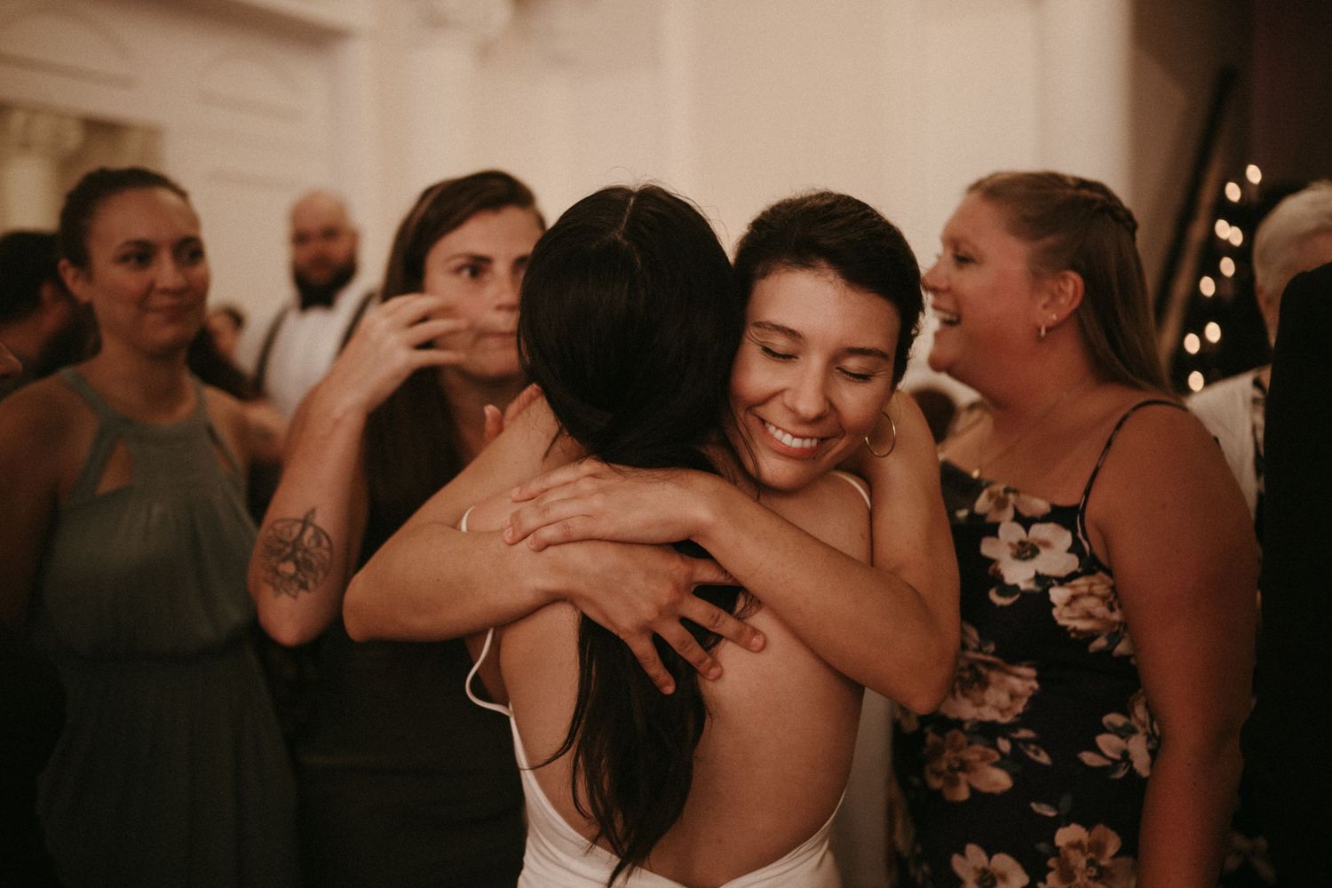 Bride shares a joyful hug with a smiling guest at a wedding reception celebration.