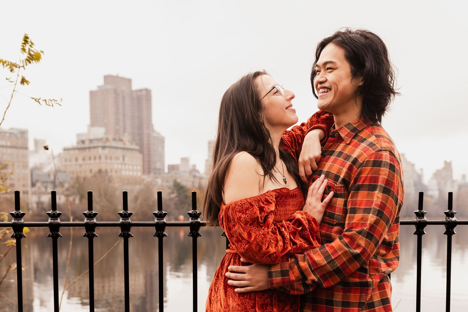Two people in orange and red outfits share a joyful moment together in Central Park during autumn.