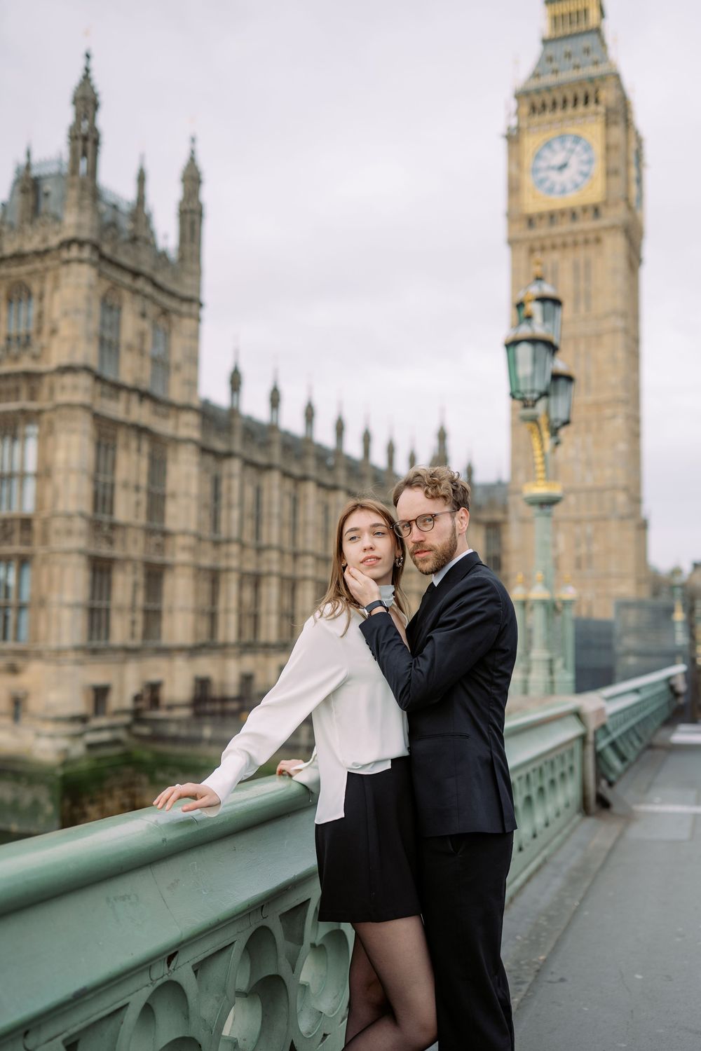 A romantic couple poses together on Westminster Bridge with Big Ben and Parliament in the background.