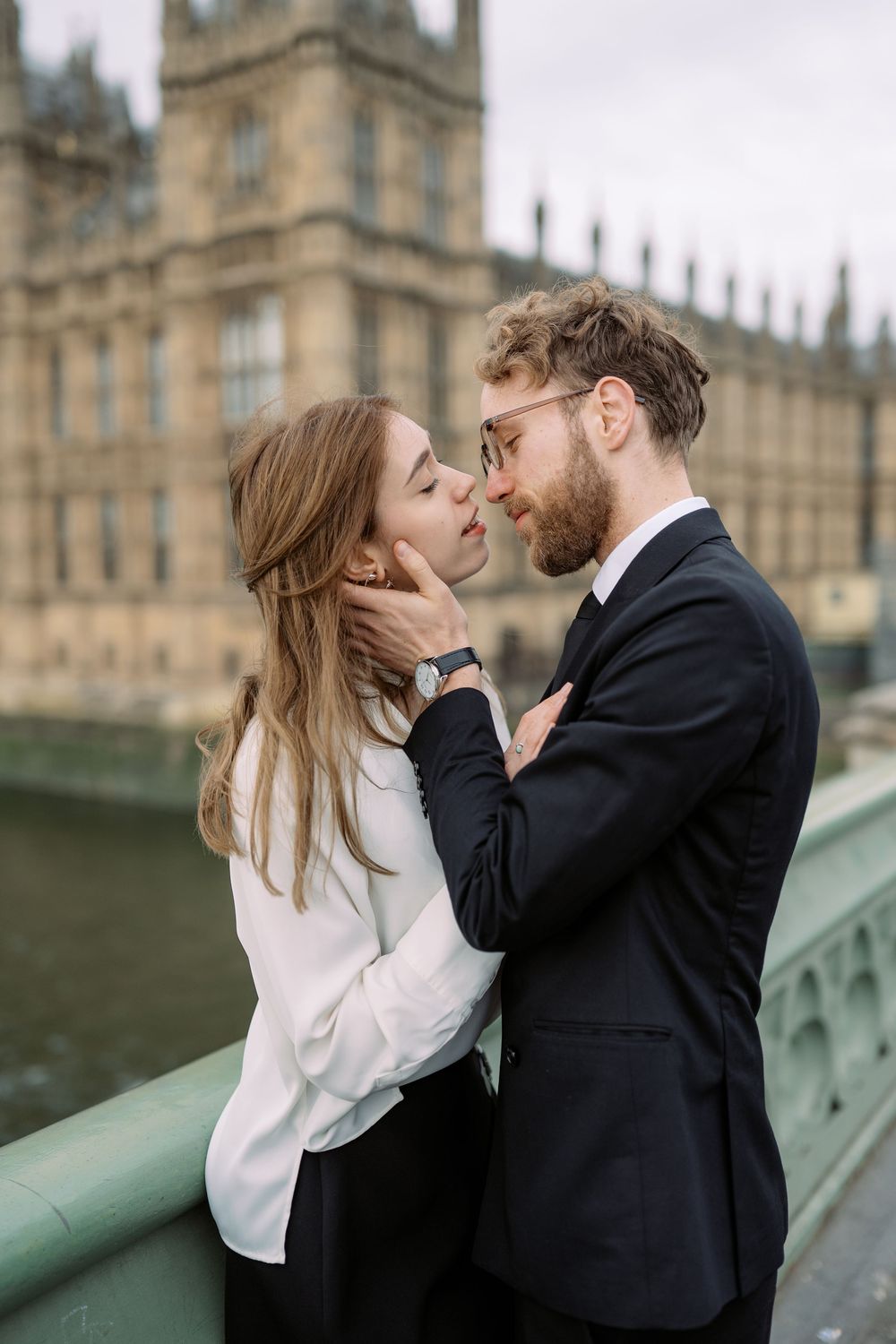 A romantic couple shares an intimate moment near Westminster Palace in London, with the iconic building in the background.