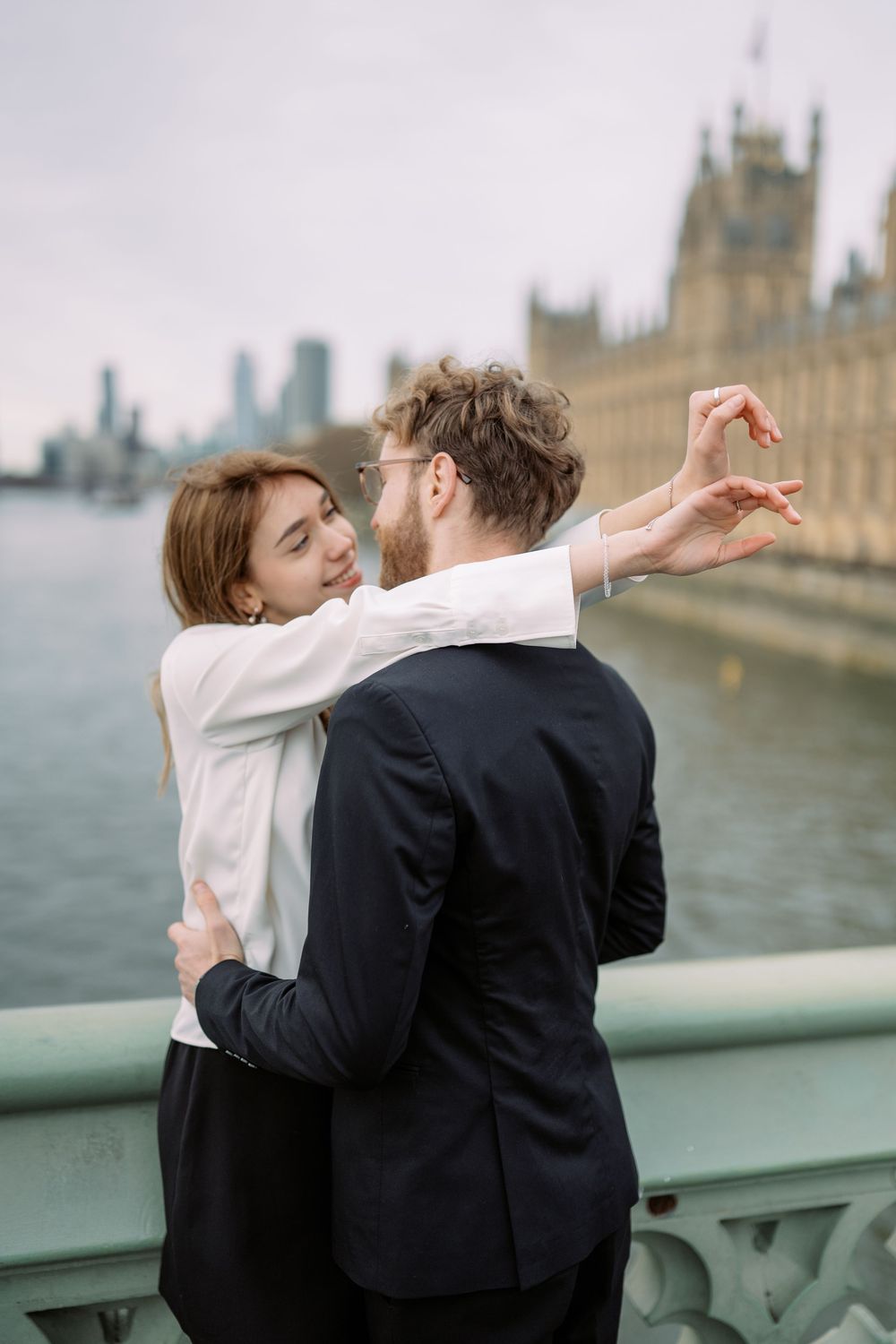 A romantic couple embraces on Westminster Bridge with the Houses of Parliament visible in the background in London.